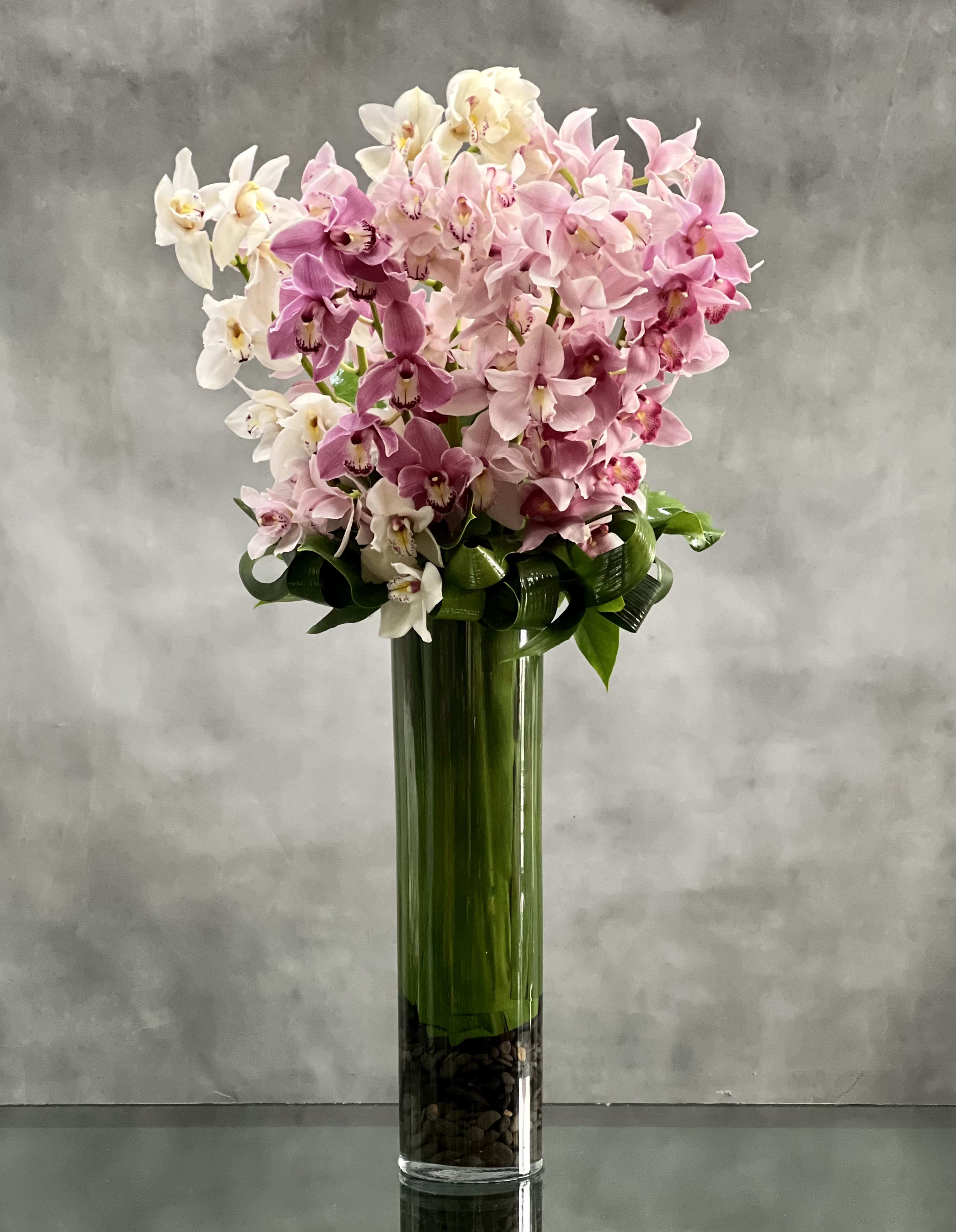 Climbing the Ladder - Sherman Oaks Florist - Deliver happiness and joy with this magnificent floral design that features a modern tall leaf lined vase overflowing with 10 tall stems of gorgeous pink, lavender and white  Cymbidium Orchids. Unique and breathtakingly beautiful!   approx 4.5 ft tall