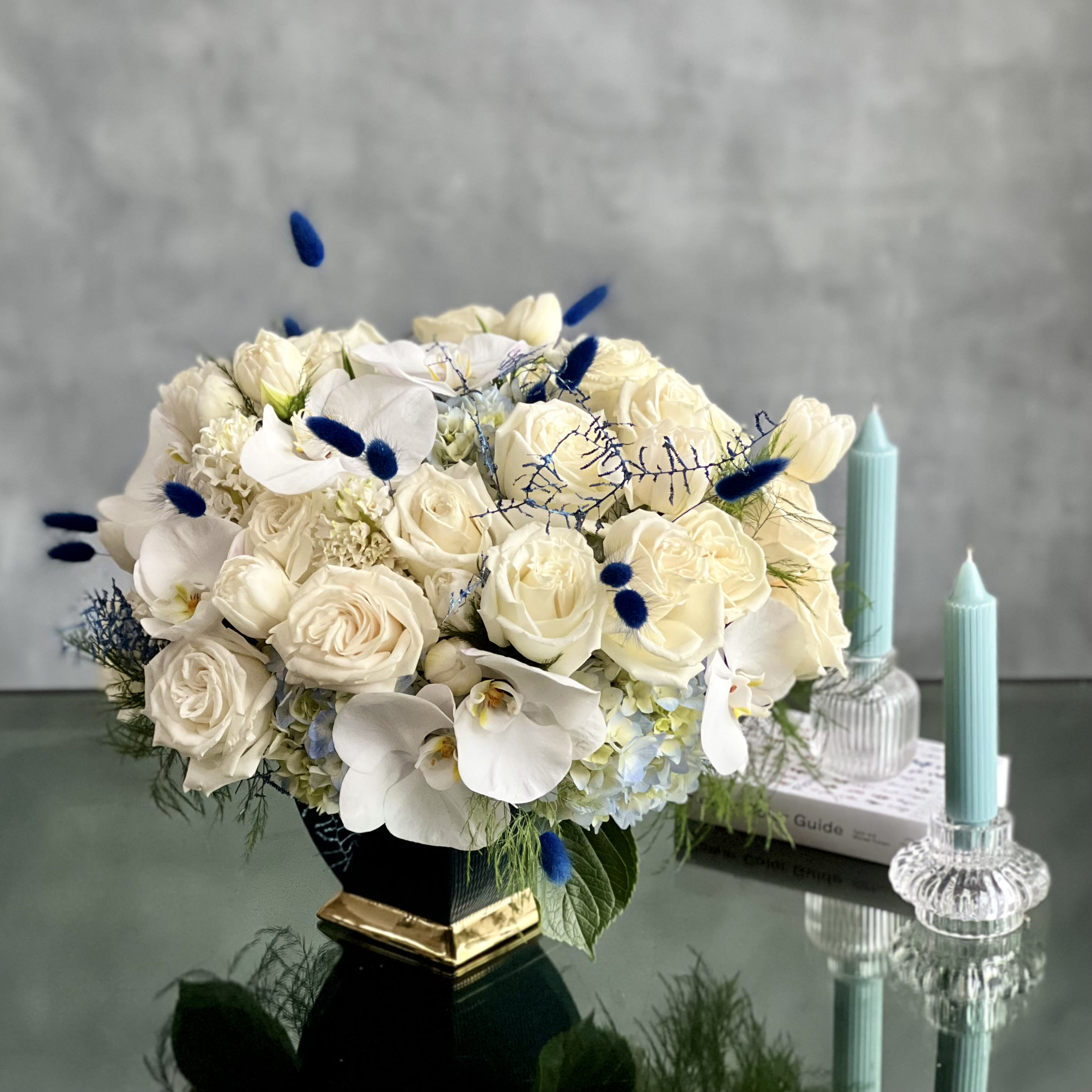 Cool Elegance - Sherman Oaks Florist - Delicate white Roses with white orchids, and hyacinths mixed with the texture and fullness of pale blue Hydrangeas in modern ceramic dark blue and gold rimmed vase. Botanical artistry and splendor at it's best!