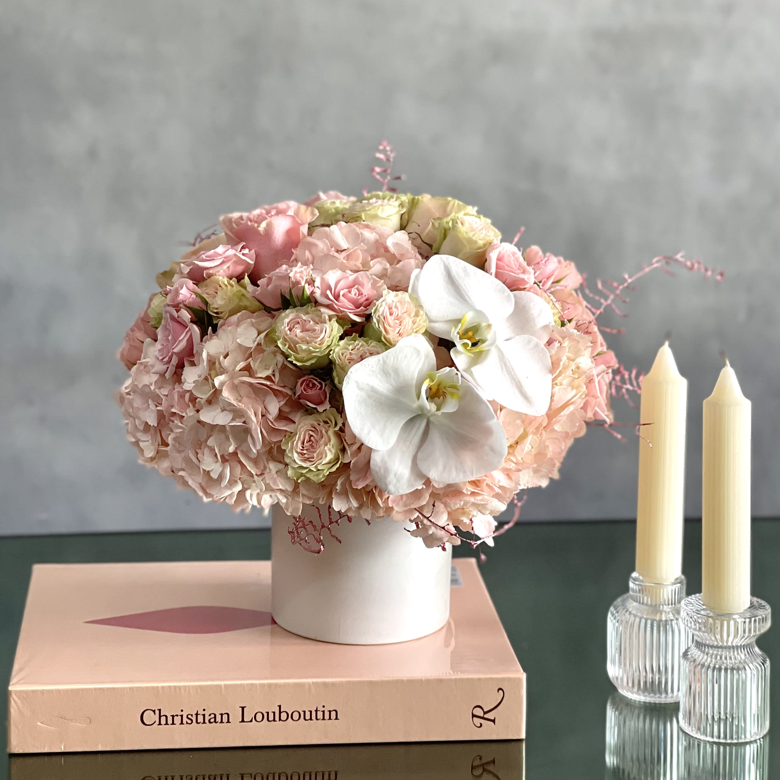 Dancing On Clouds  - A soft and chic arrangement made of Pink Hydrangeas, Roses and Spray Roses, with a touch of white Orchids. Which is then placed in a white ceramic vase. With its soft Pinks and its touch of white Orchids, it can make anyone smile ! 
