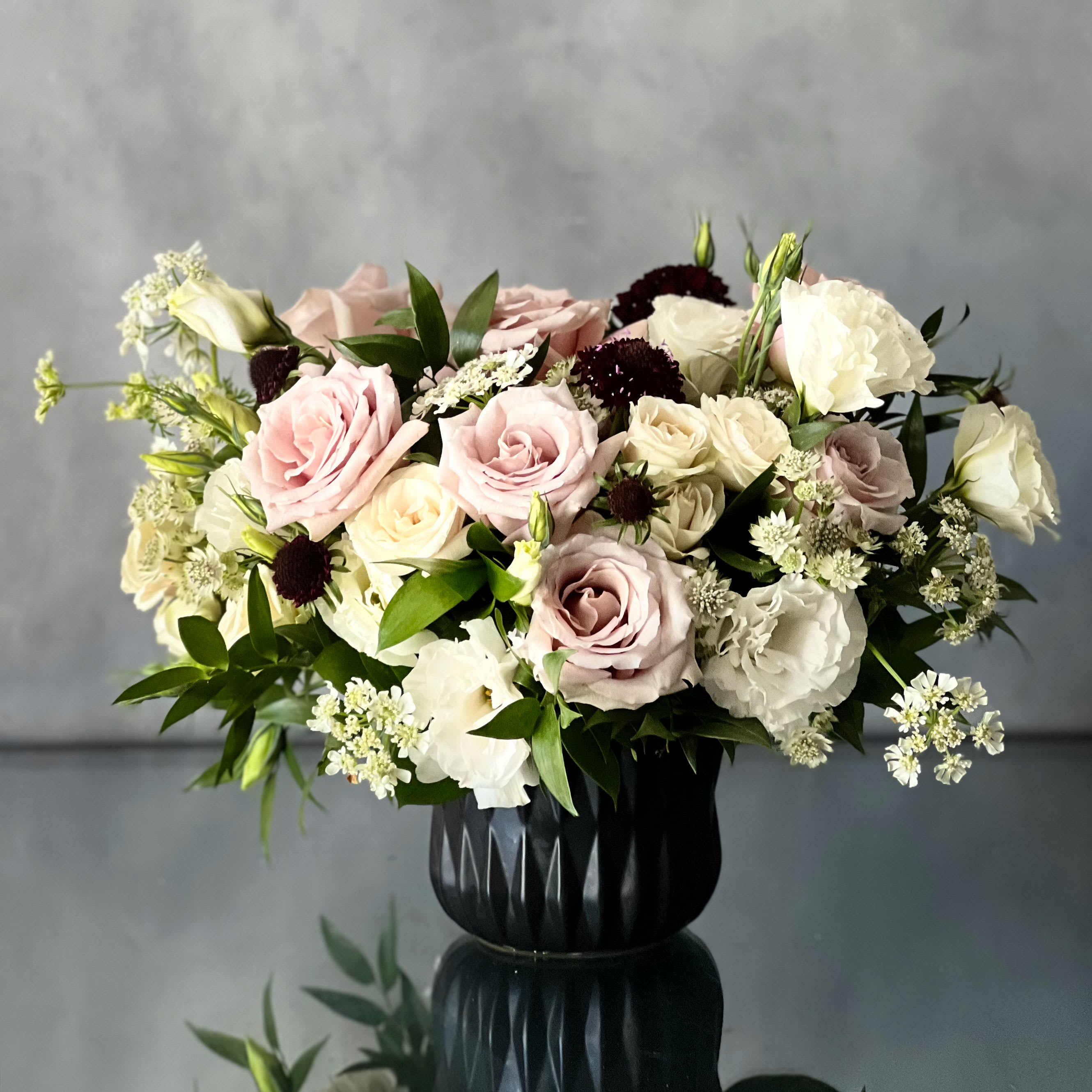 Dreamy - Our beautiful arrangement consists of White and light lavender Roses, Thistles and other seasonal florals placed within a matte black geometric vase.. Wonderful for a Thank You, Just Because or Thinking Of You. A romantic bouquet to delight the senses and commemorate any special moment. Perfect for expressing your appreciation or just sending a bit of cheerfulness.  AS SHOWN PREMIUM
