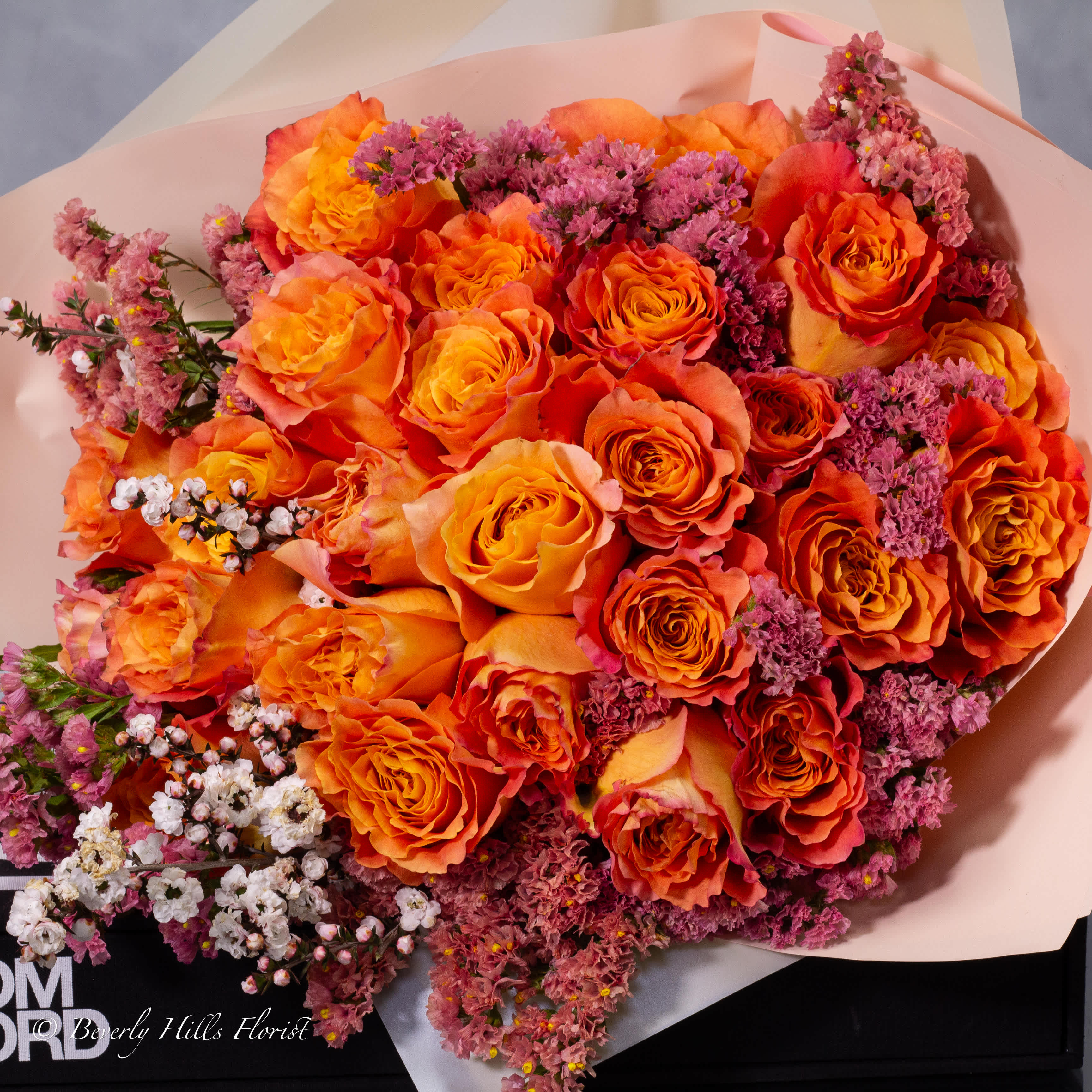 Bouquet of orange roses with pink filler flowers wrapped in pale pink paper