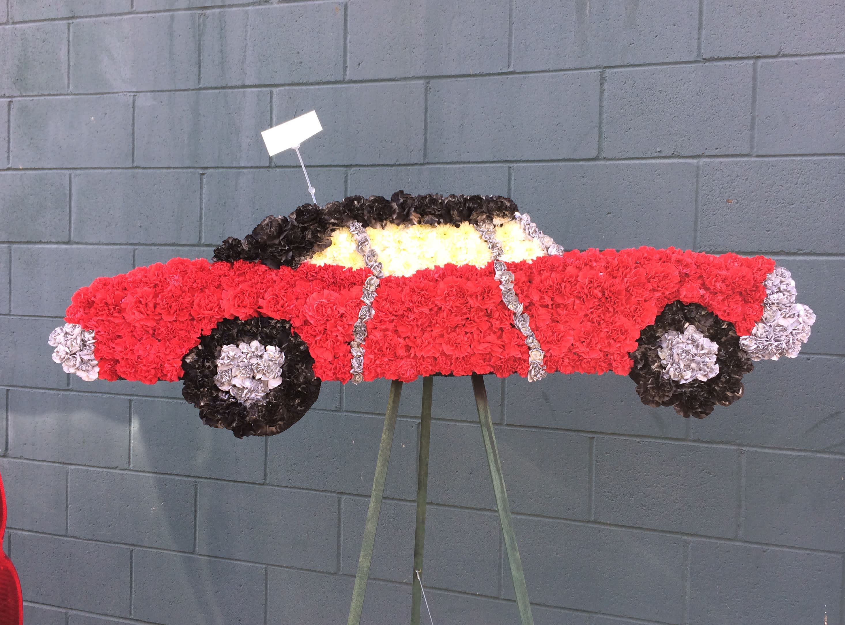 Floral arrangement shaped like a red car on a stand