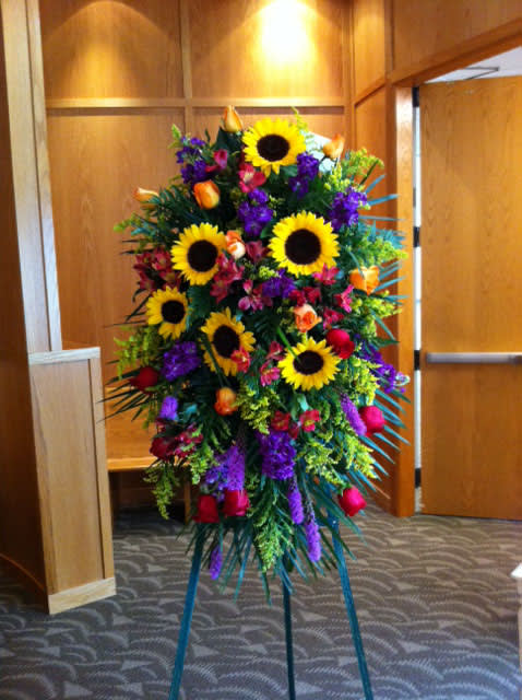 Tall standing floral spray with sunflowers, roses, and purple blooms