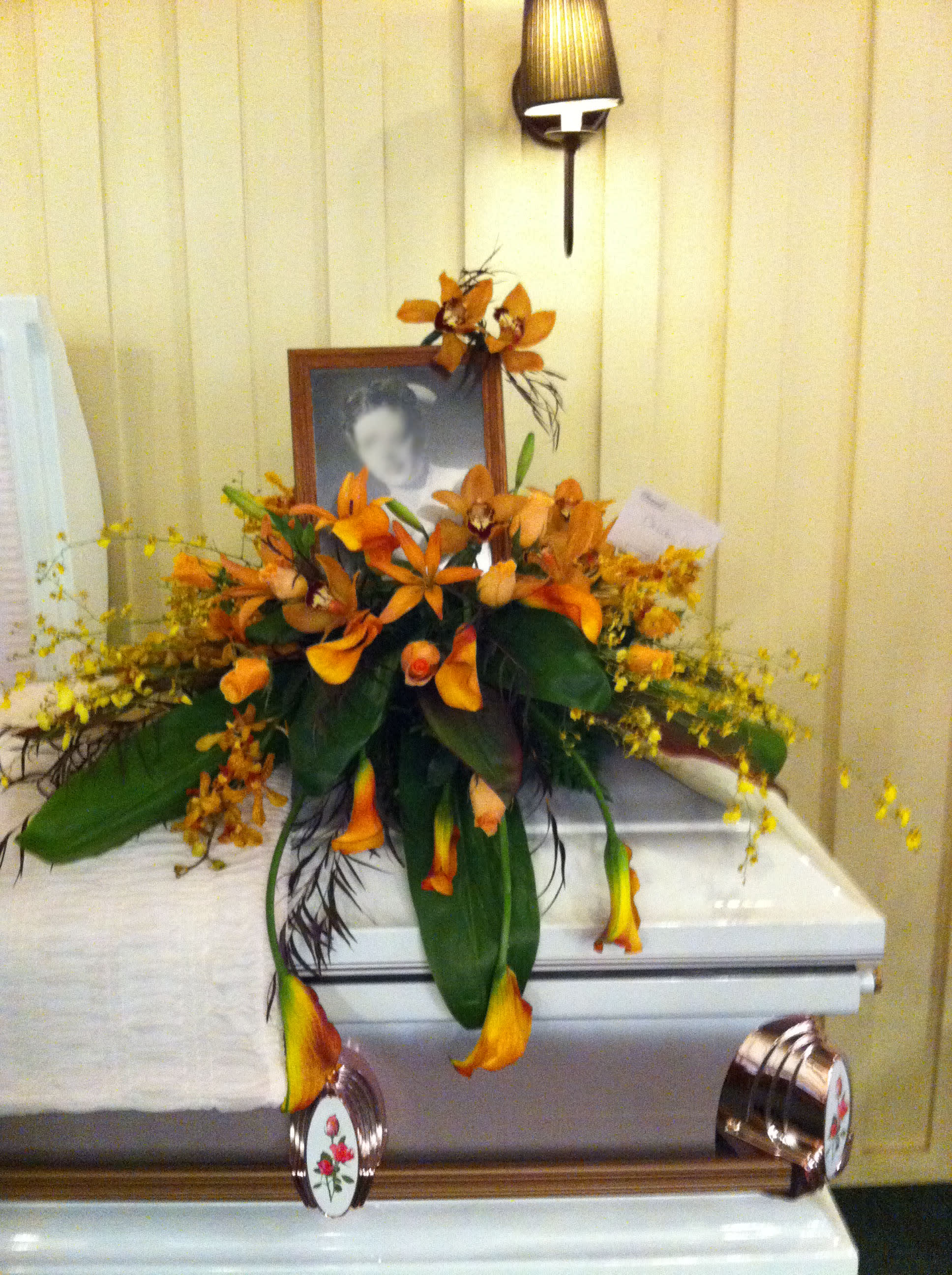 Orange floral arrangement on a white casket with a framed photo