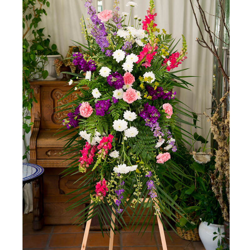 Tall standing spray of pink, white, and purple flowers with abundant greenery on a wooden easel