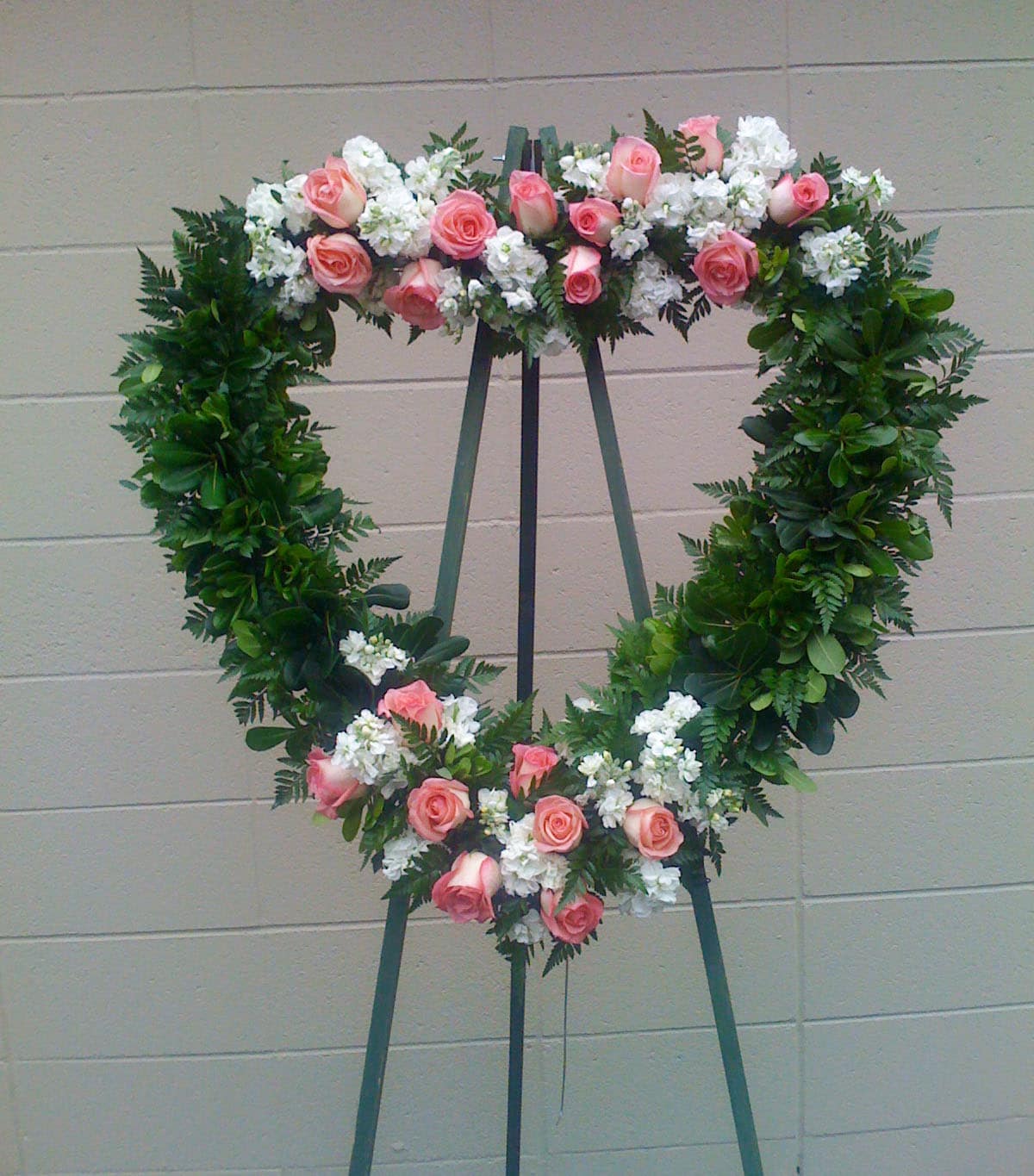 Heart-shaped floral wreath with pink roses and white flowers on an easel