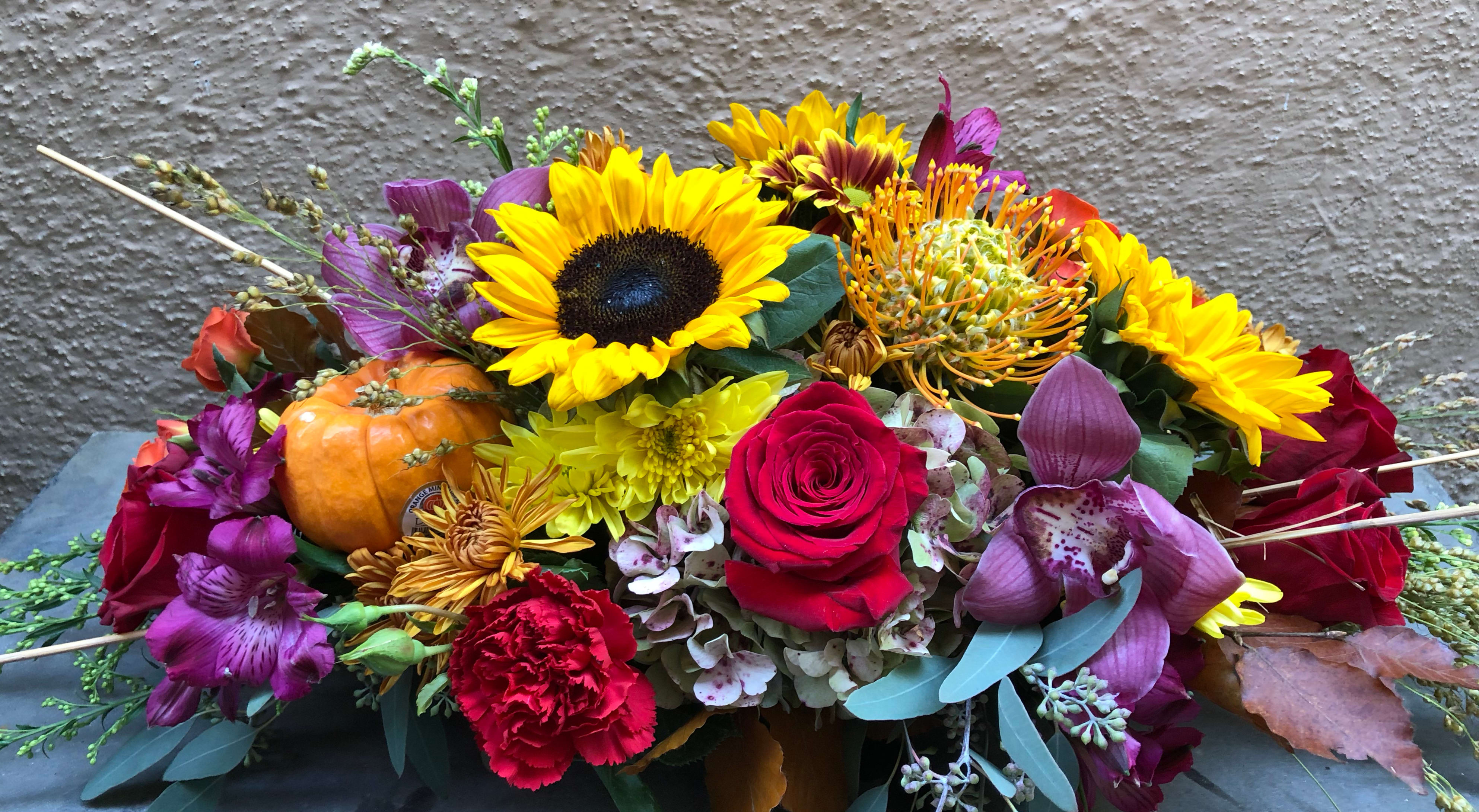 Mixed floral arrangement with sunflowers, roses, orchids, and a small pumpkin