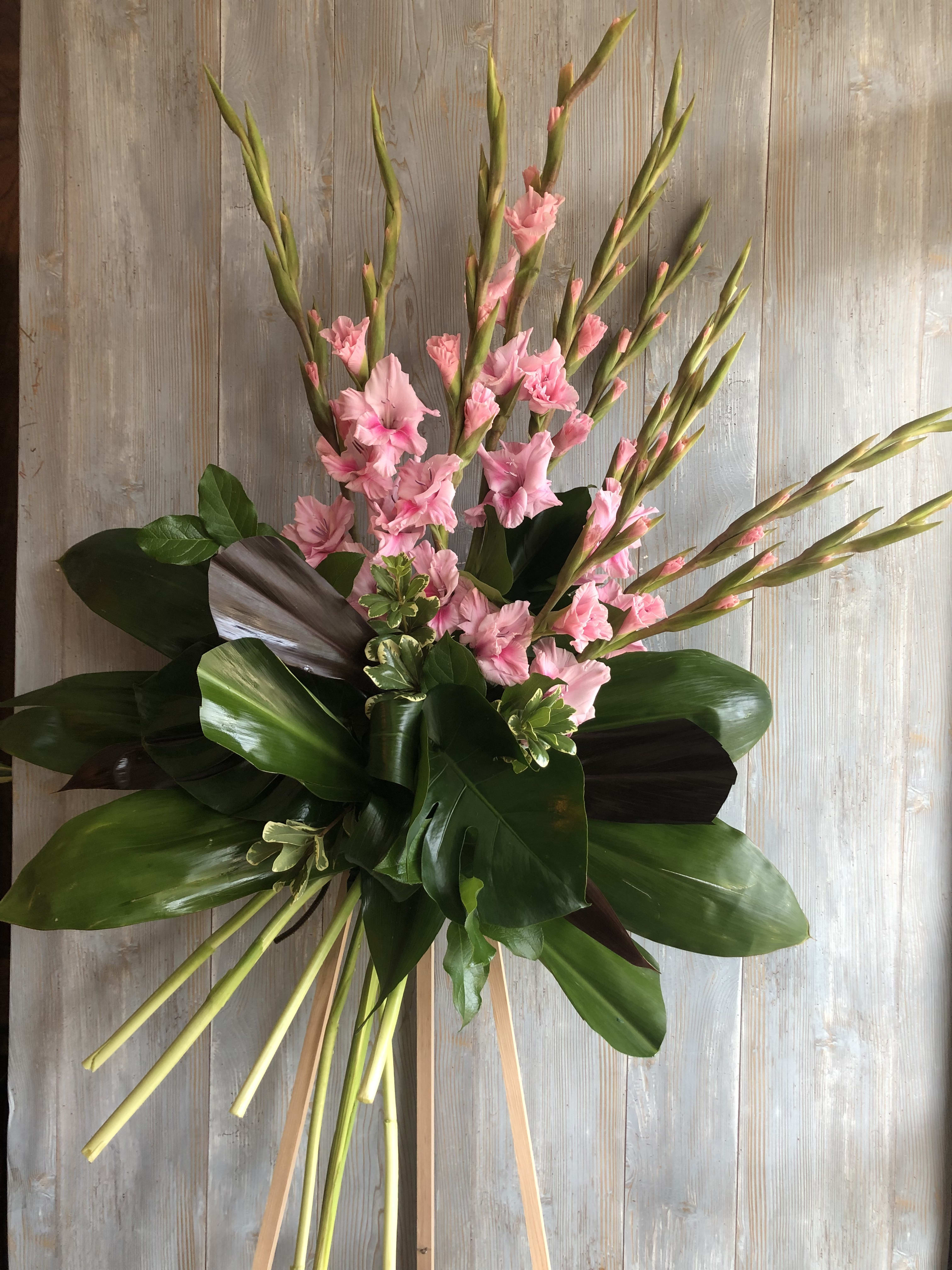 Tall arrangement of pink flowers with large glossy leaves on a wooden stand