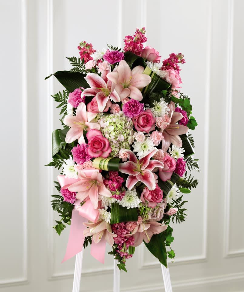 Standing spray of pink lilies, roses, carnations, and white daisies on an easel.