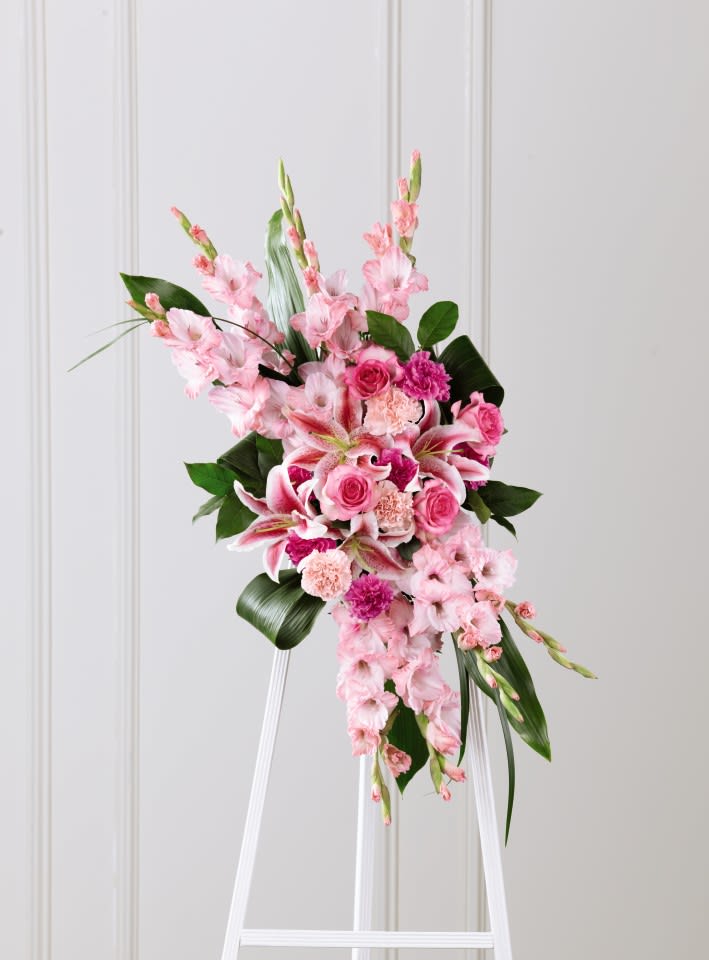 Tall pink standing floral spray on a white easel with roses, lilies, and carnations.