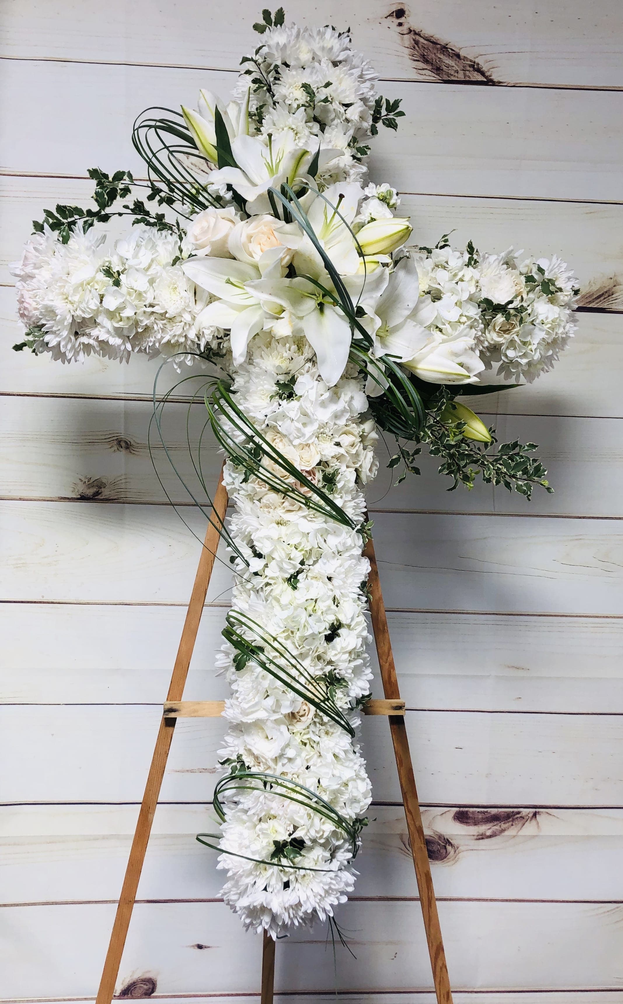White floral cross arrangement on a wooden easel