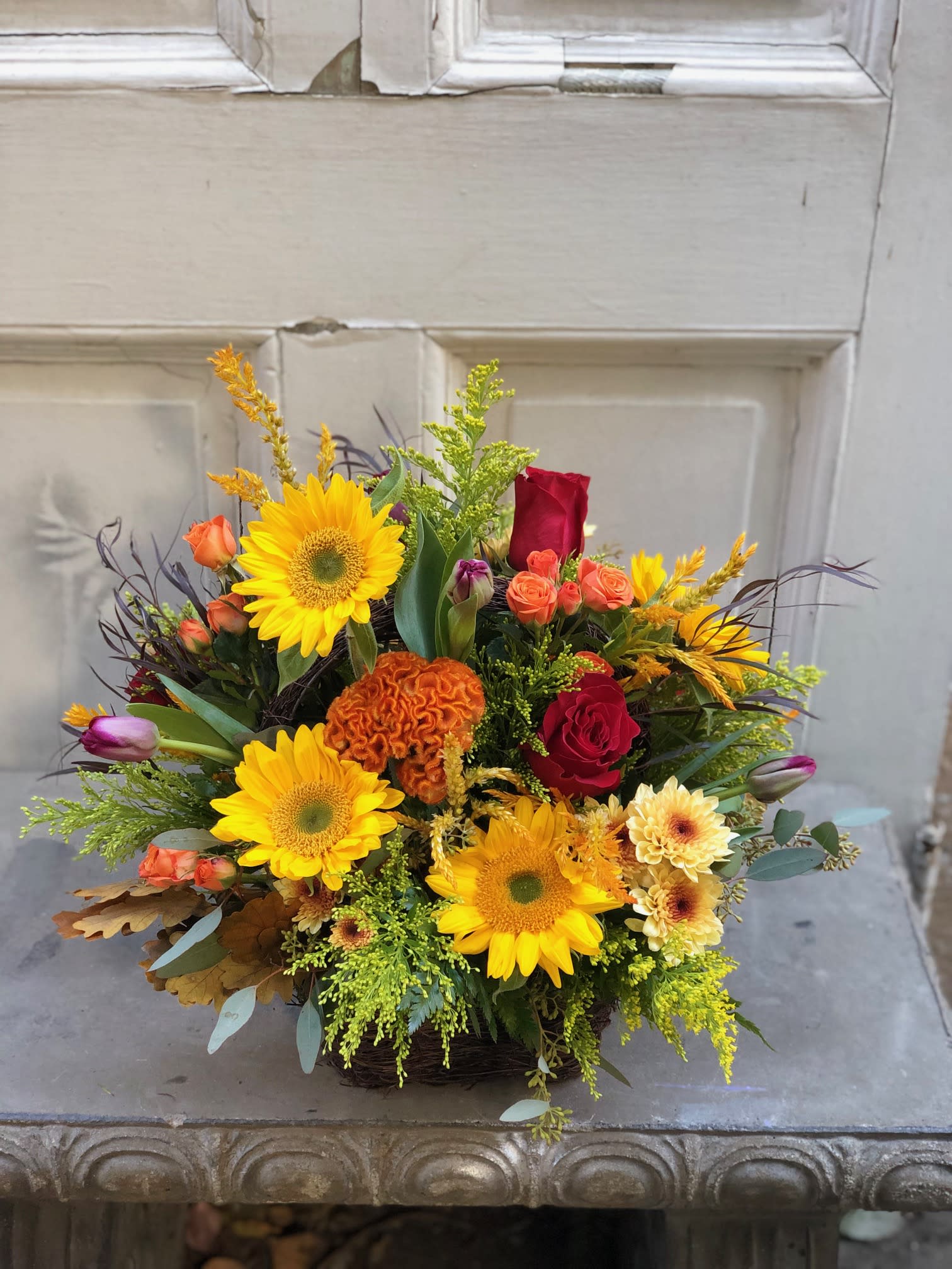 Mixed bouquet with sunflowers, red roses, and orange blooms in a basket