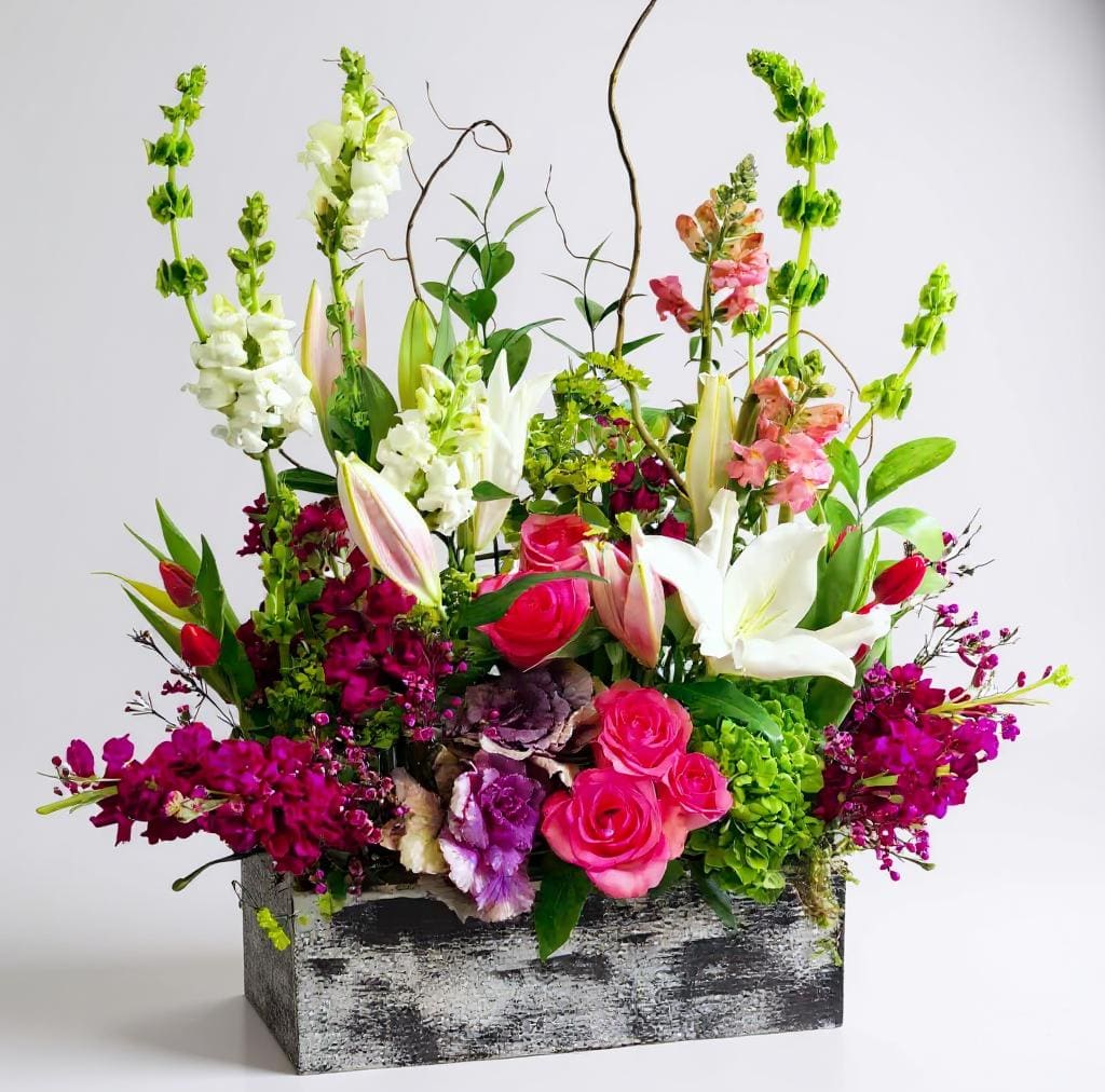 Mixed floral arrangement with pink roses, white lilies, and tall snapdragons in a rustic box