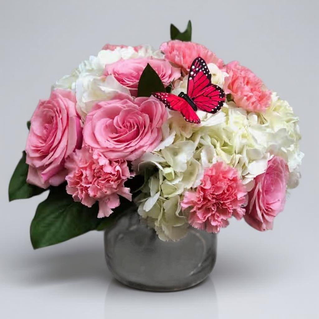 Pink and white flower arrangement in a glass vase with a butterfly accent