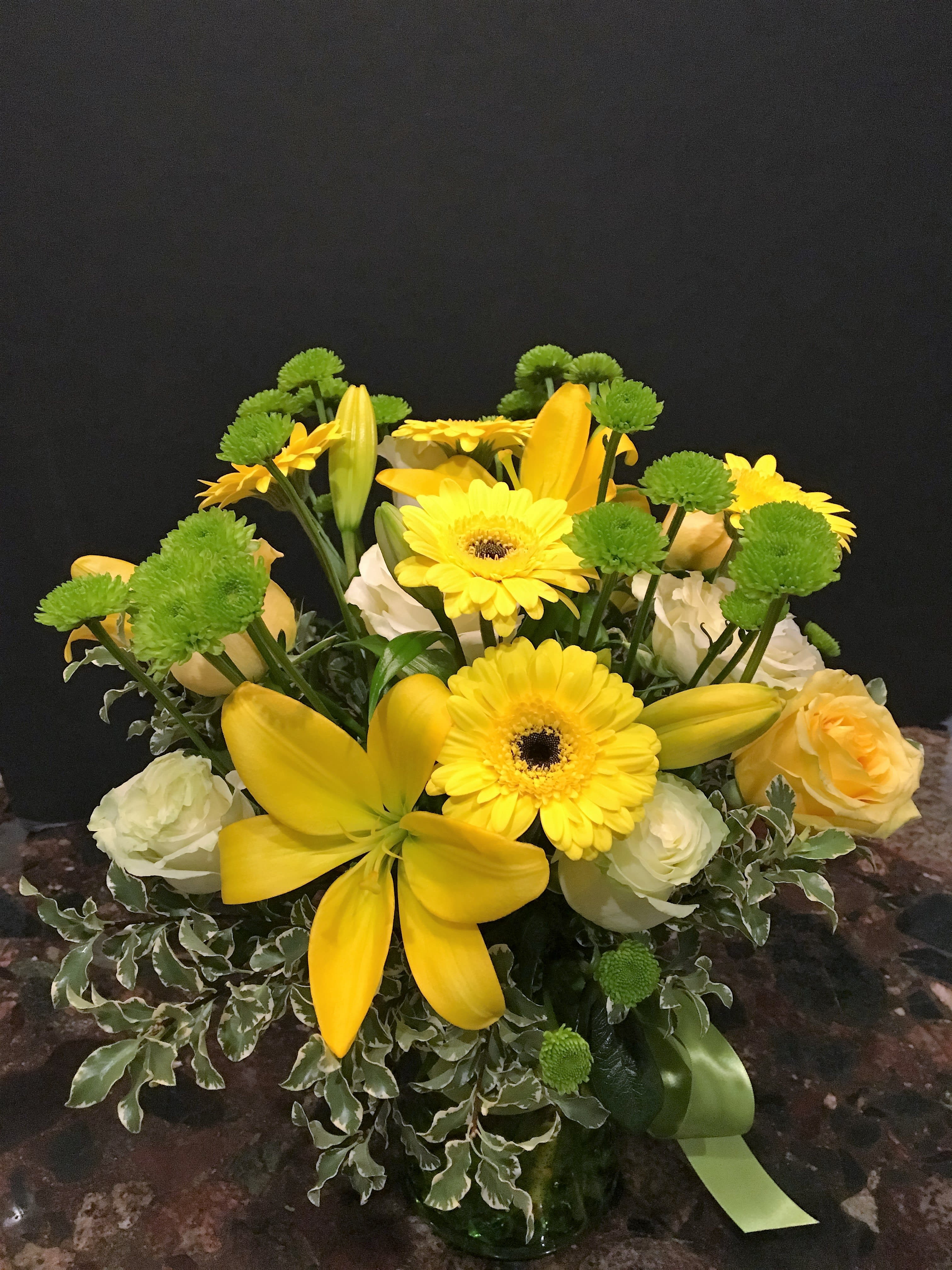 Yellow lilies and gerbera daisies with green button mums in a vase
