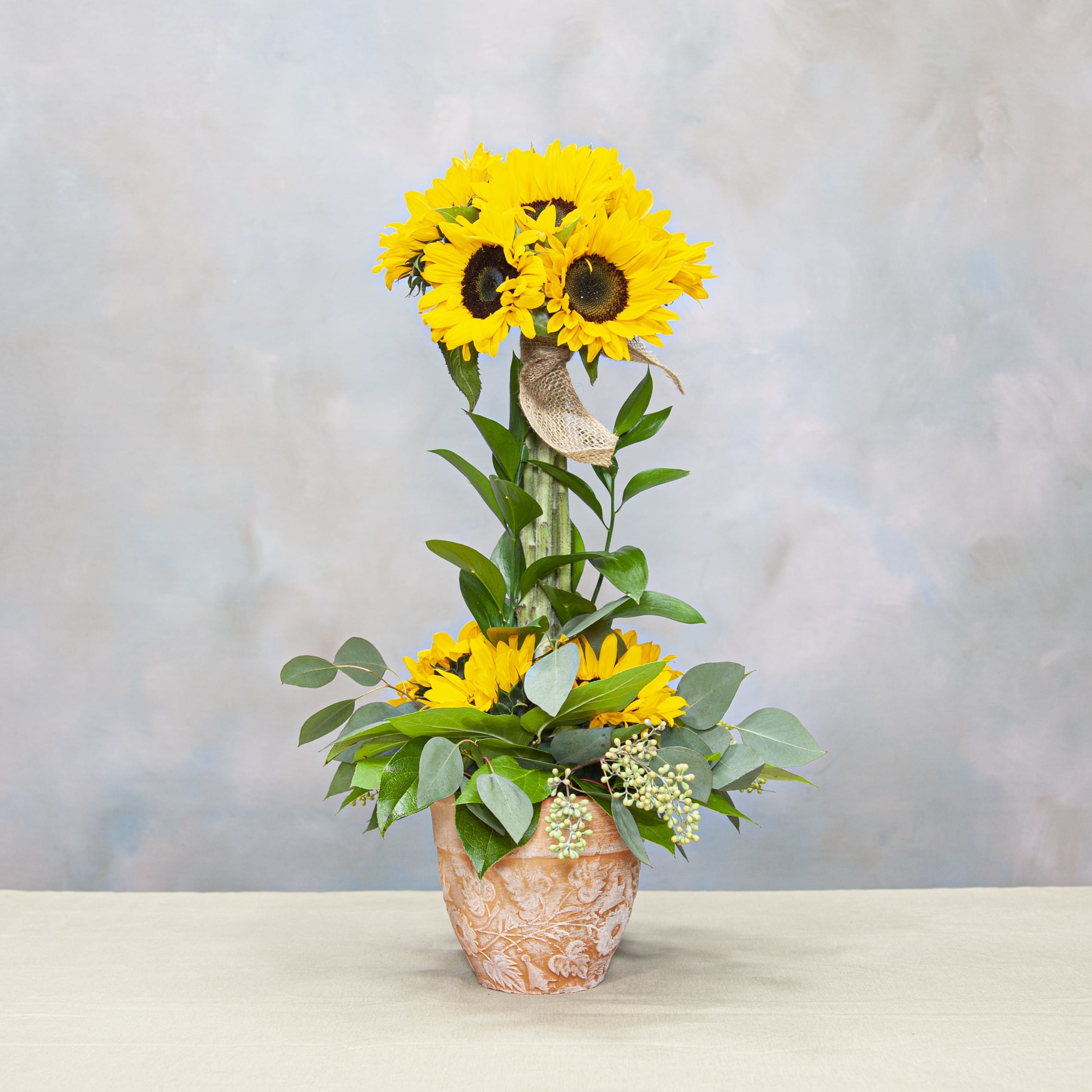 Sunflower arrangement in a textured terracotta pot with a burlap ribbon