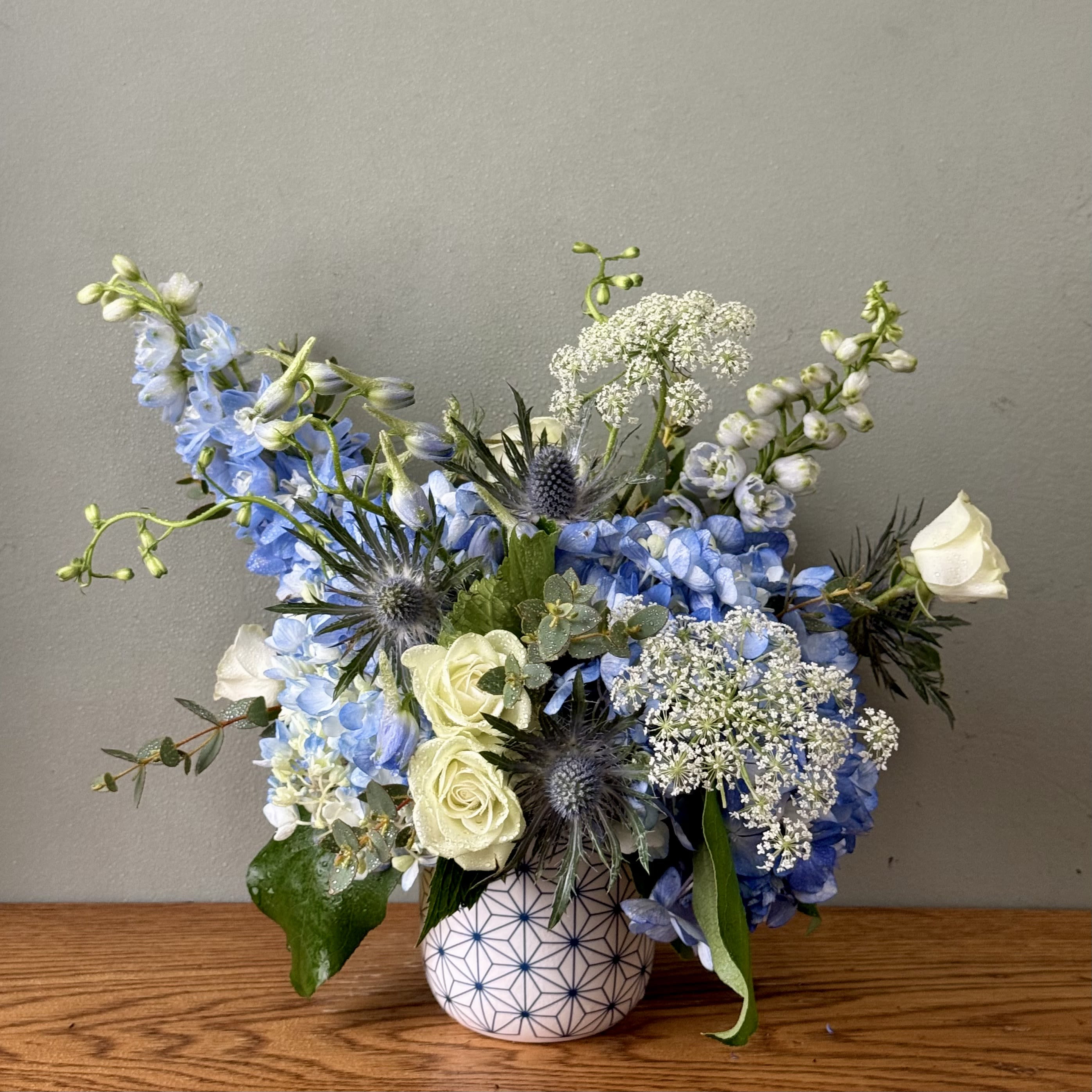 Blue and white mixed flower arrangement in a patterned vase