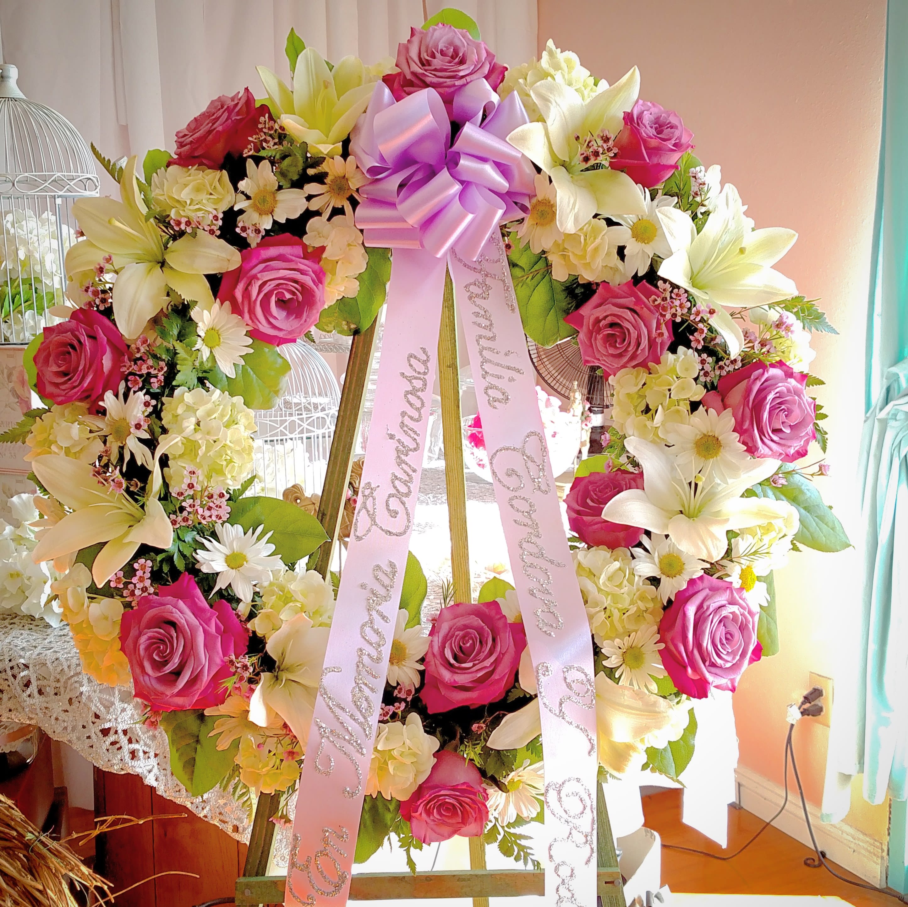 Large floral wreath with pink roses, white lilies, and a lavender ribbon bow