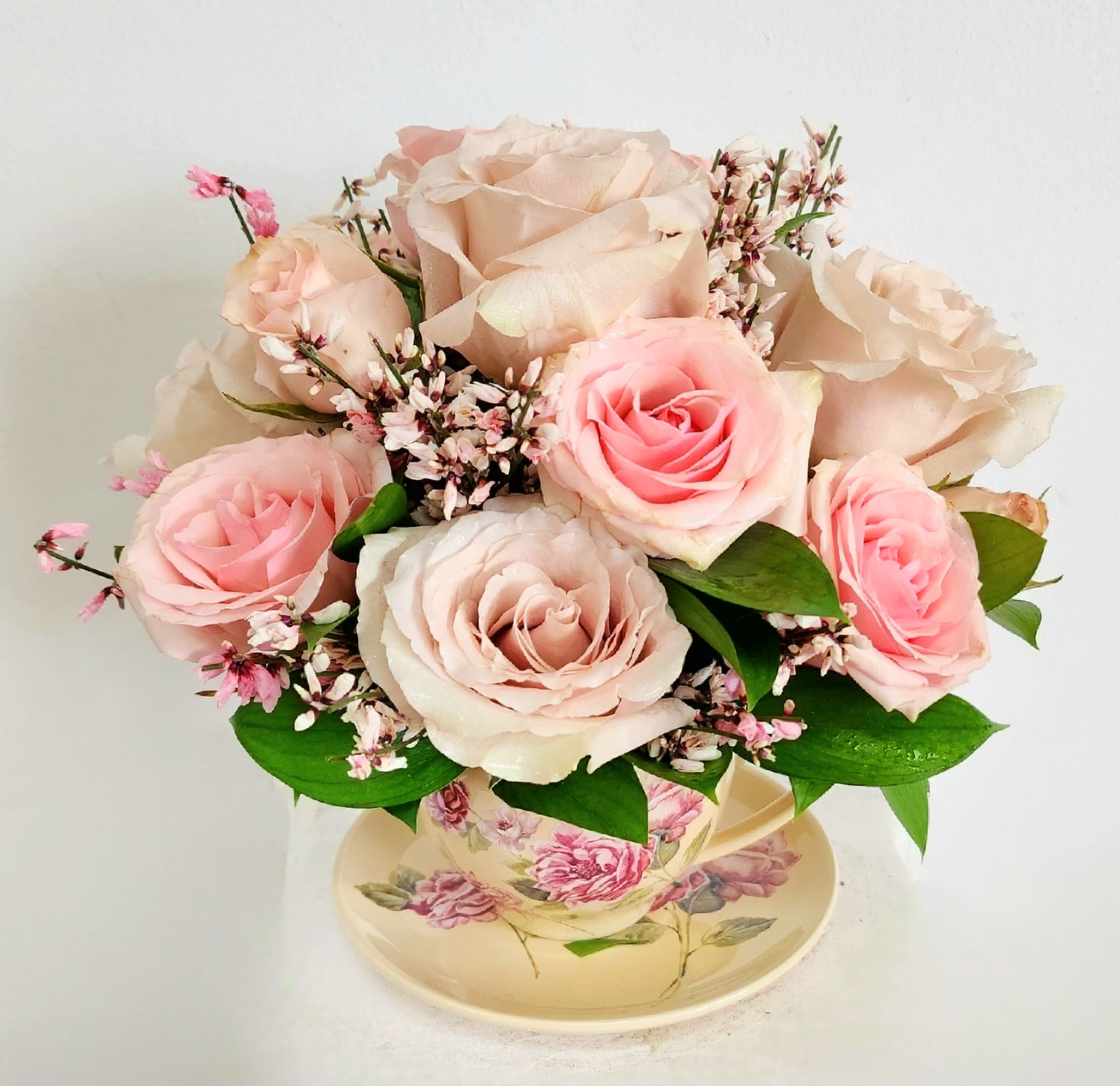 Pink and blush roses arranged in a floral teacup with a saucer