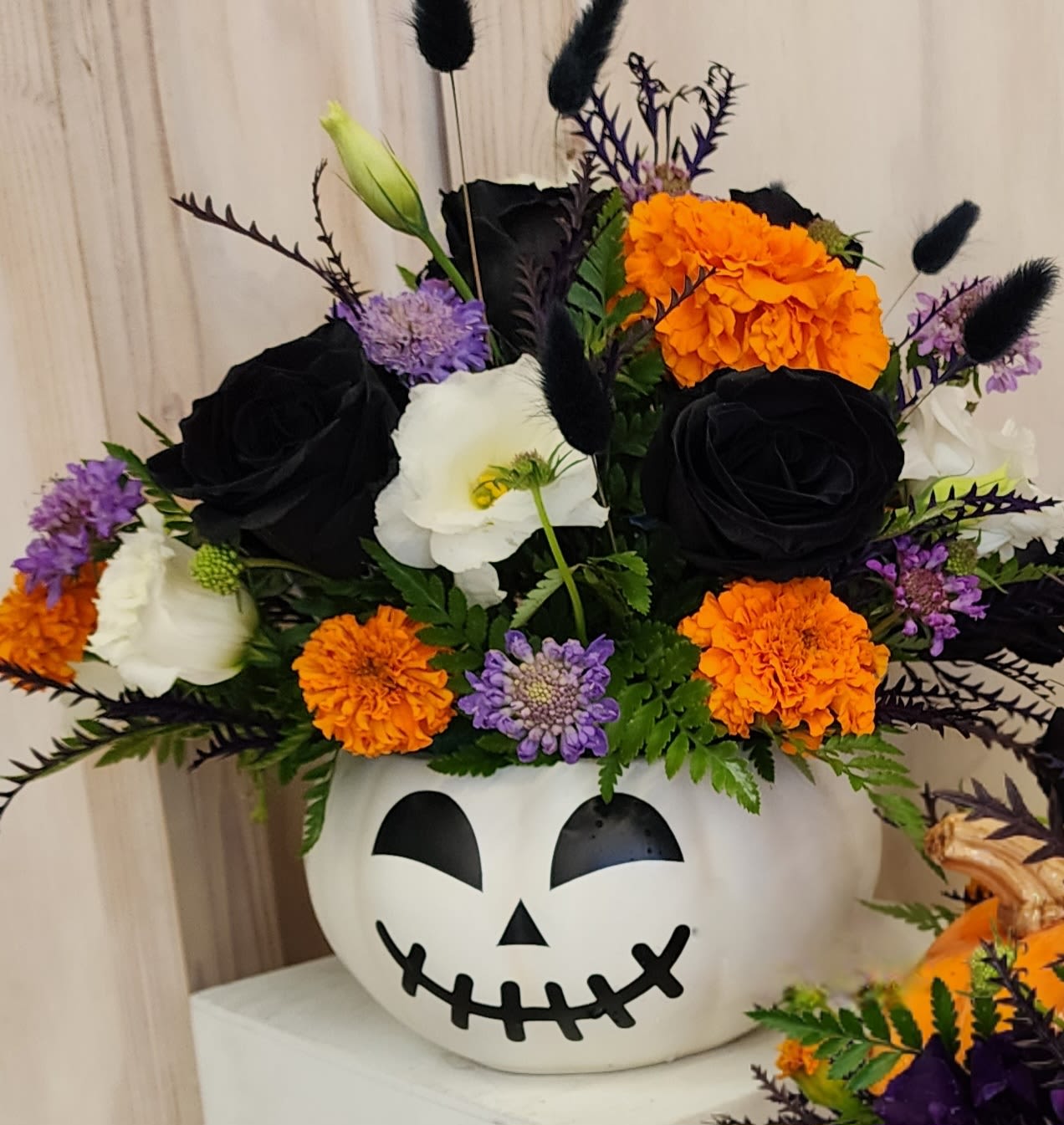 Halloween flower arrangement in a jack-o'-lantern container with black, orange, white, and purple blooms.