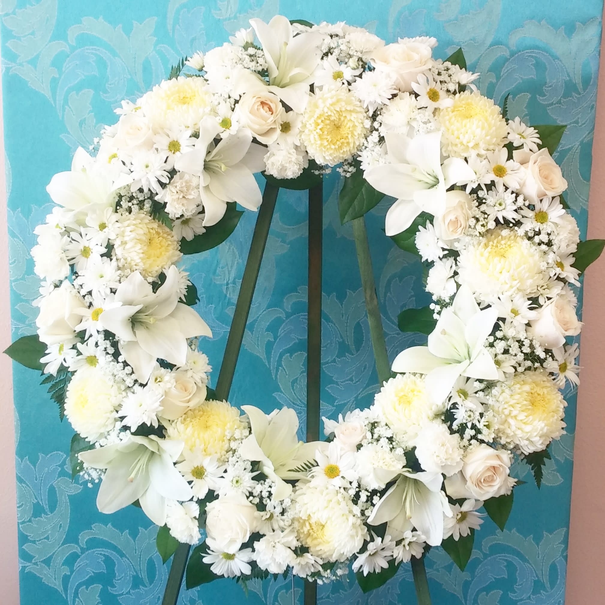 White floral wreath on a stand against a blue patterned background