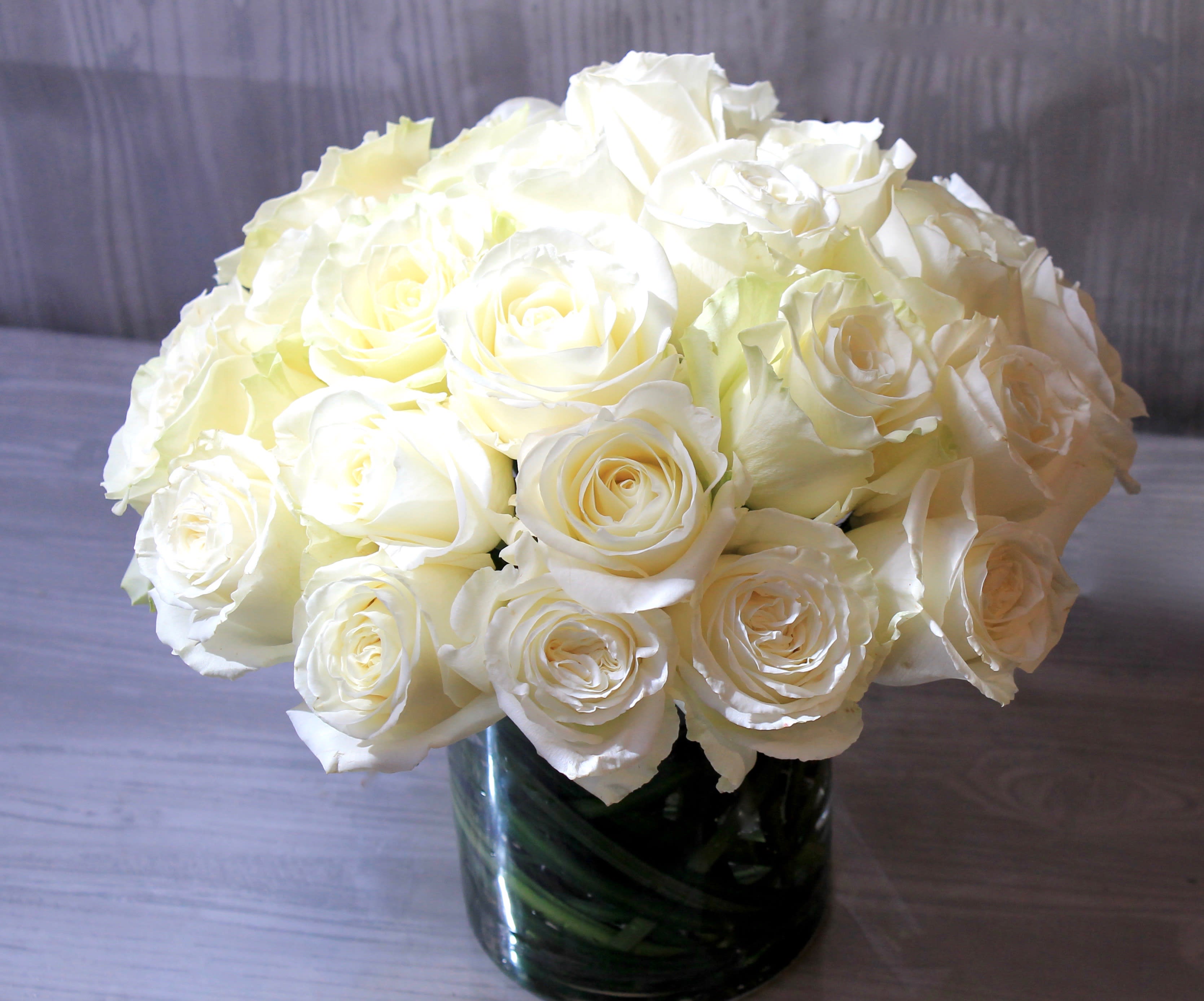 Two Dozen White Roses - Make a bold statement with this elegantly simple design. White roses symbolize hope, honor, adoration, and innocence. Two Dozen White Roses is the perfect gift to welcome new beginnings or show your respects. A classic design to send your love or sympathy wishes. Send the best flowers from the best flower shop in New York. We offer same day flower delivery in Manhattan, Queens, Bronx, Brooklyn, Staten Island and West Chester counties. We have the prettiest and most luxurious flowers to choose from and our designs are unique and whimsical. We carry Peonies almost every day of the year!!#mercuryvase #weddingflowers #luxuryflowers #ranunculus #peony #peonies #flowerdelivery #samedaydelivery #funeralflowers   Arrangement Details: 2 dozen white roses in a glass cylinder vase.  APPROXIMATE DIMENSIONS are 11"D X 12"H