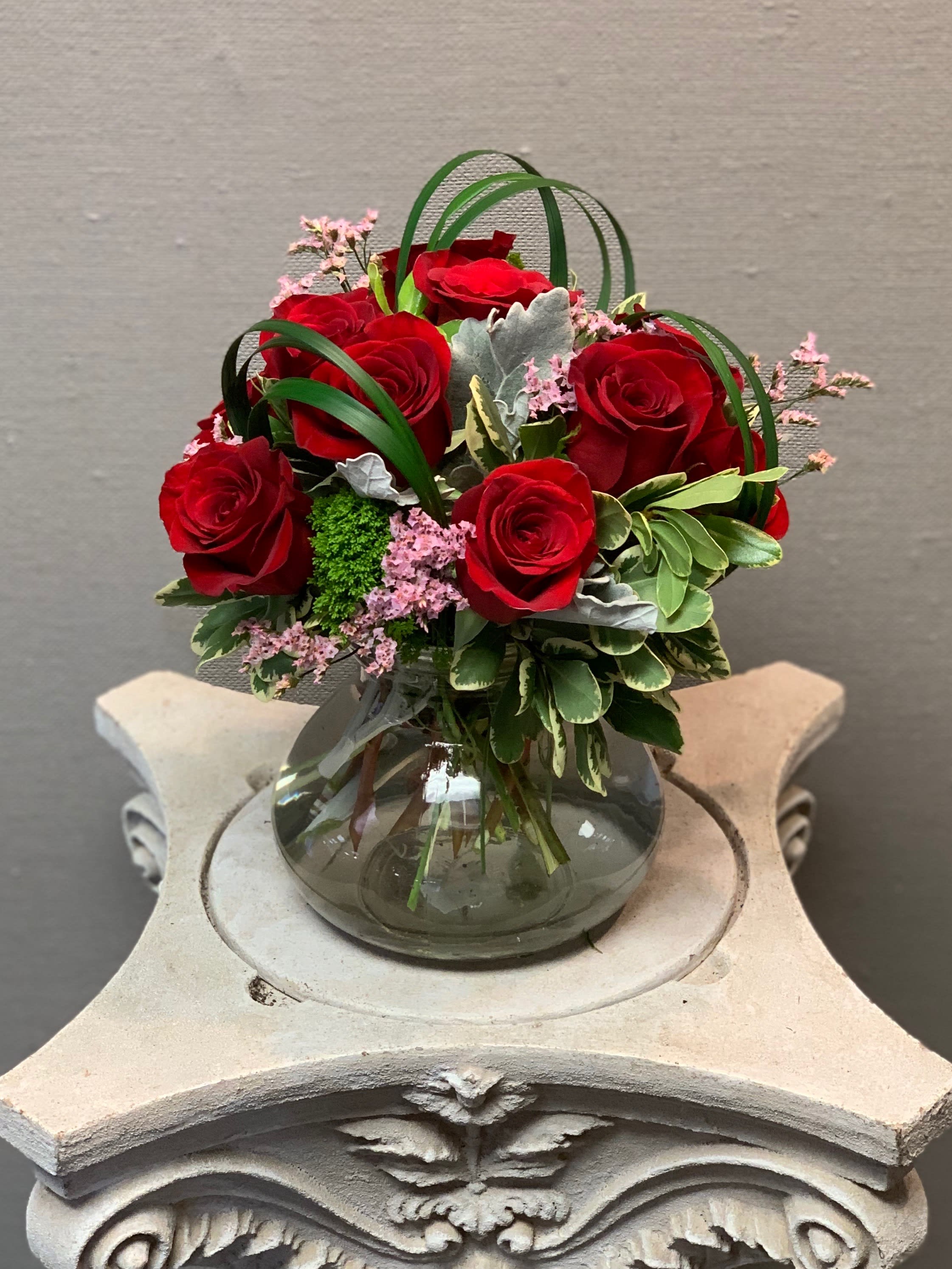 Red roses arranged in a glass vase with pink filler flowers