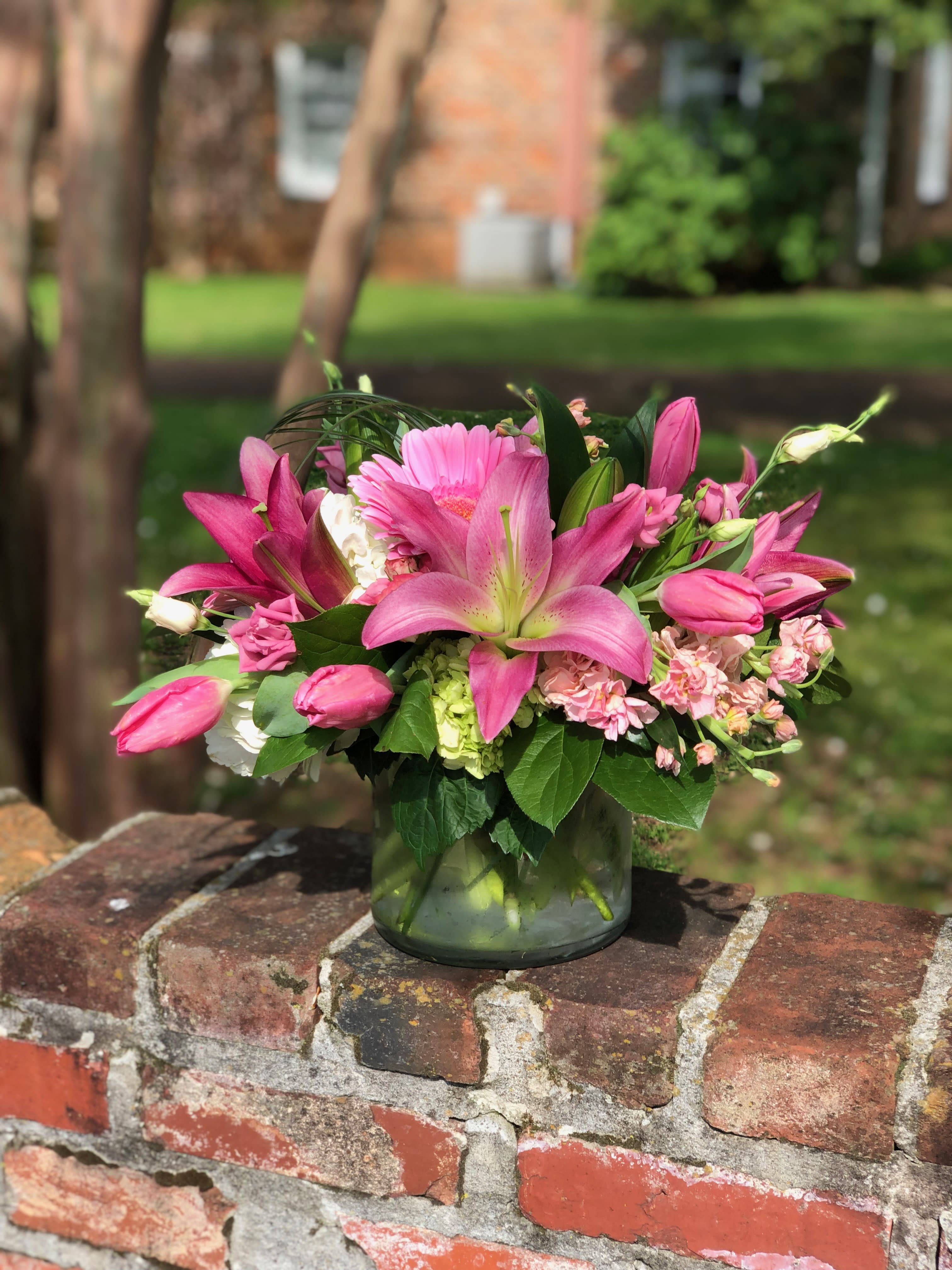 Pink lilies and mixed blooms arranged in a glass vase