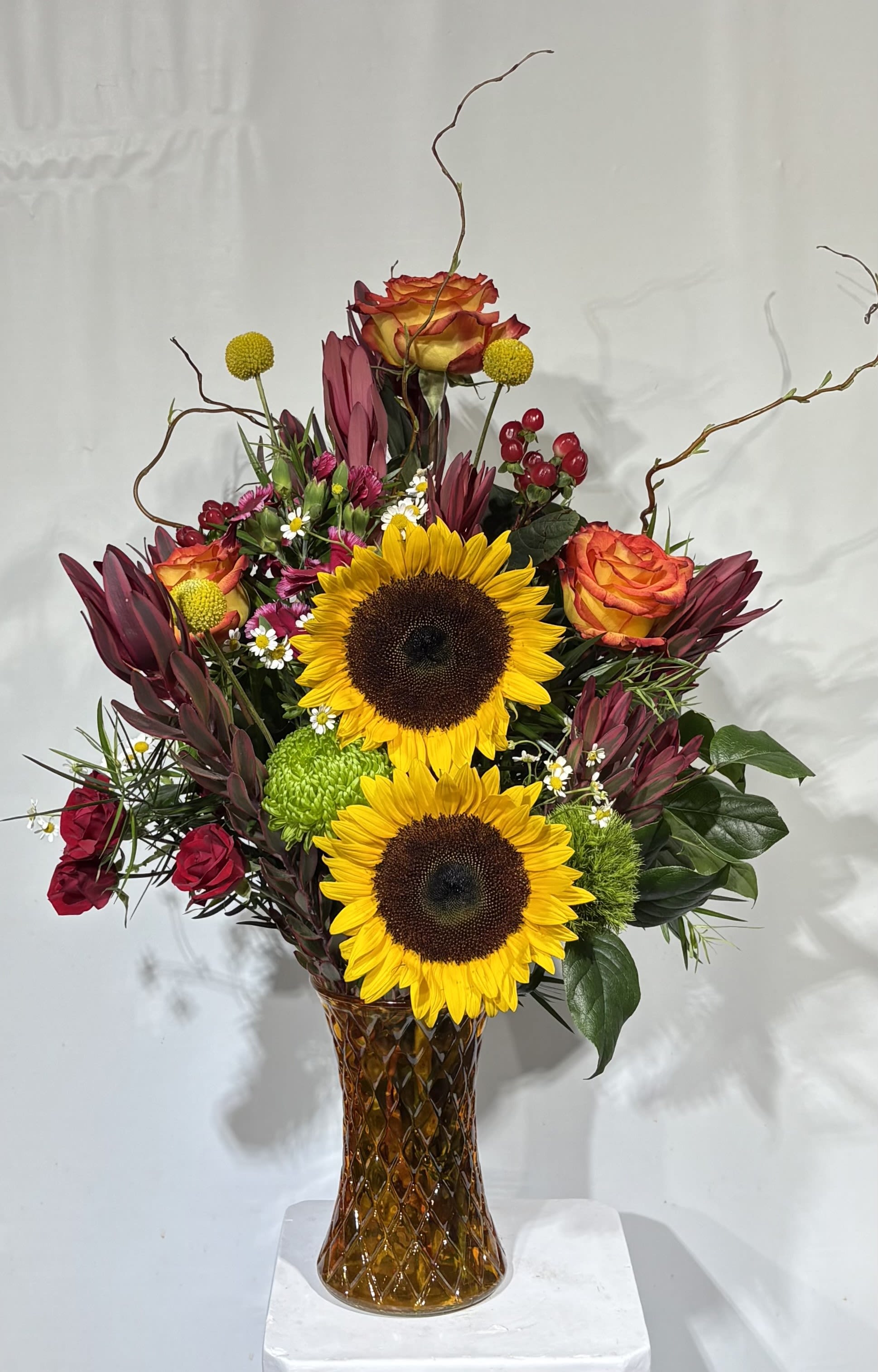 Sunflowers and roses arranged in a tall amber glass vase