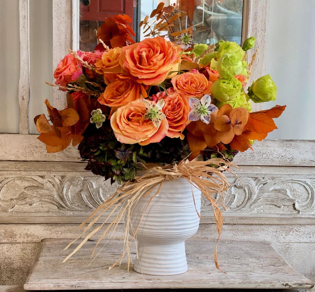 Orange and pink roses in a white vase with dried accents