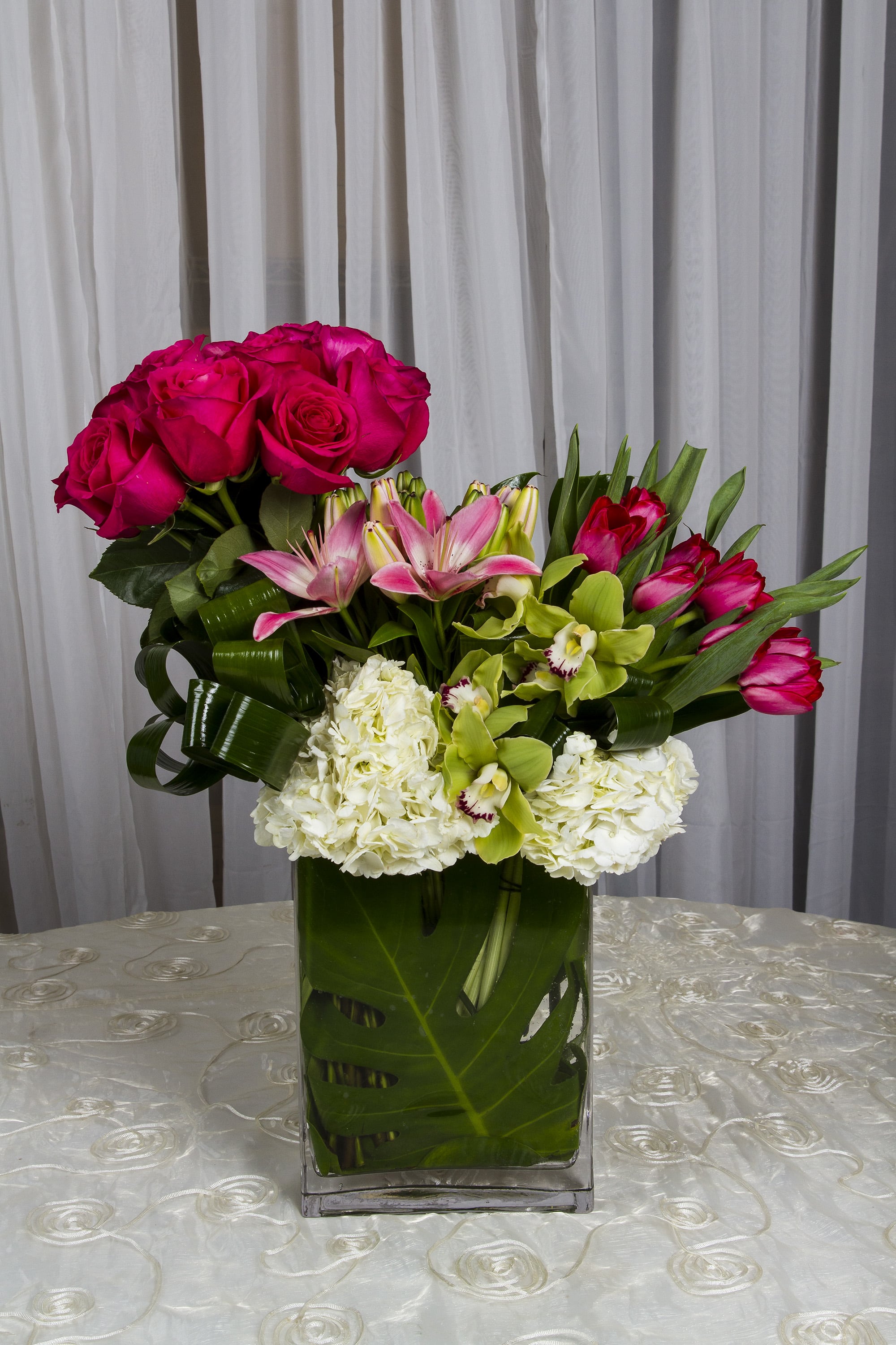 Pink roses, lilies, orchids, and white hydrangeas in a glass vase