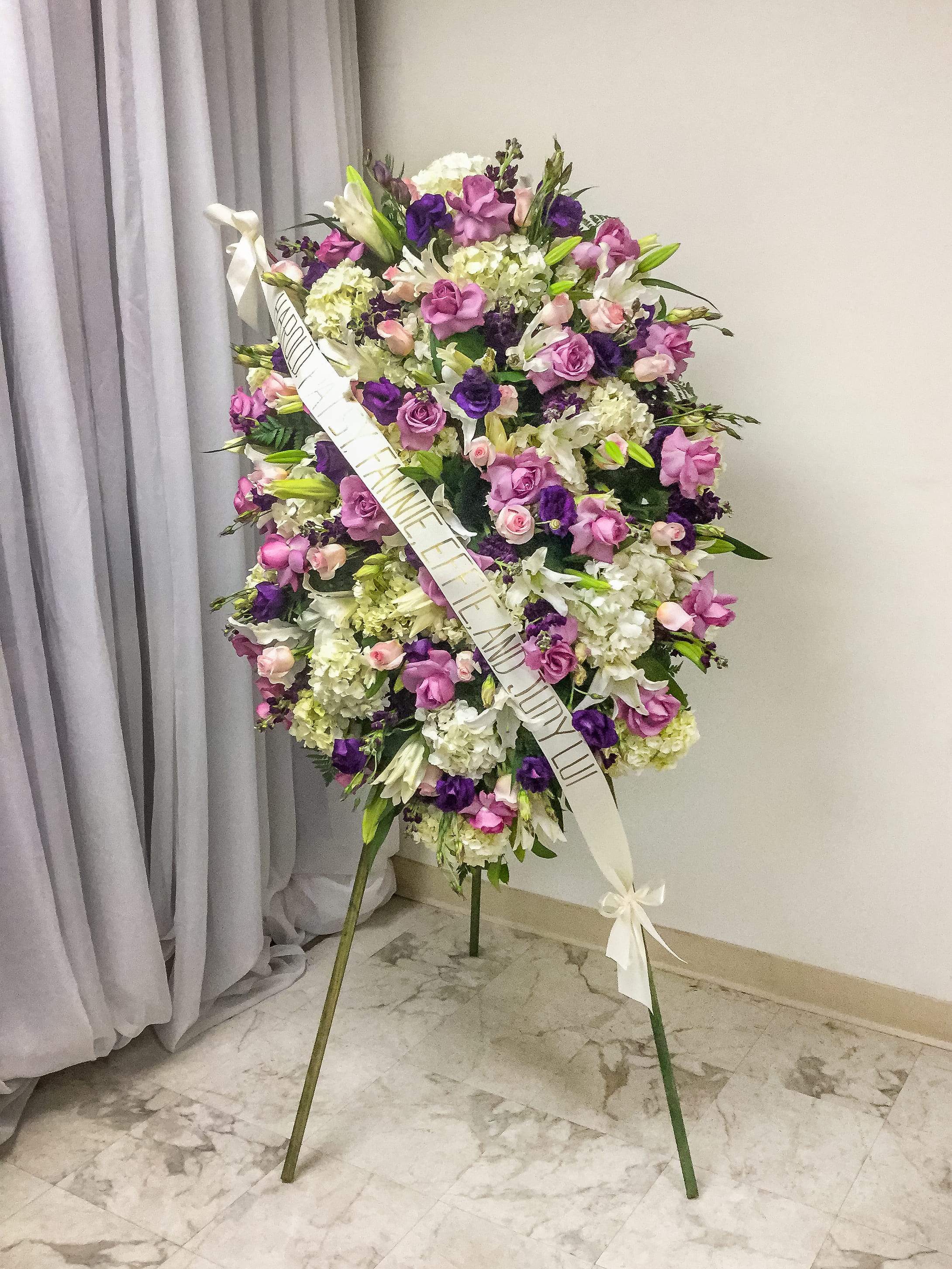 Large standing floral spray in purple, pink, and white with a ribbon