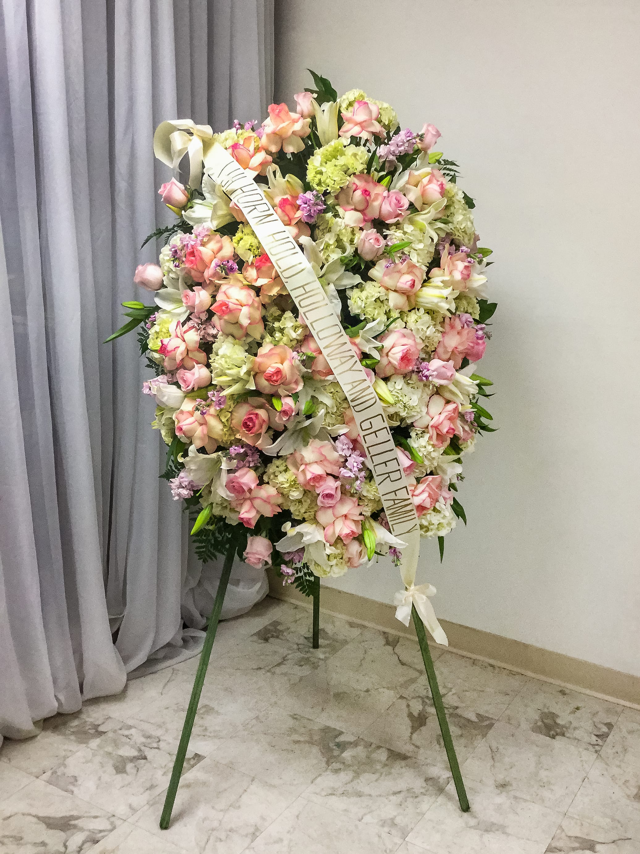 Standing funeral wreath of pink and white flowers with a condolence ribbon