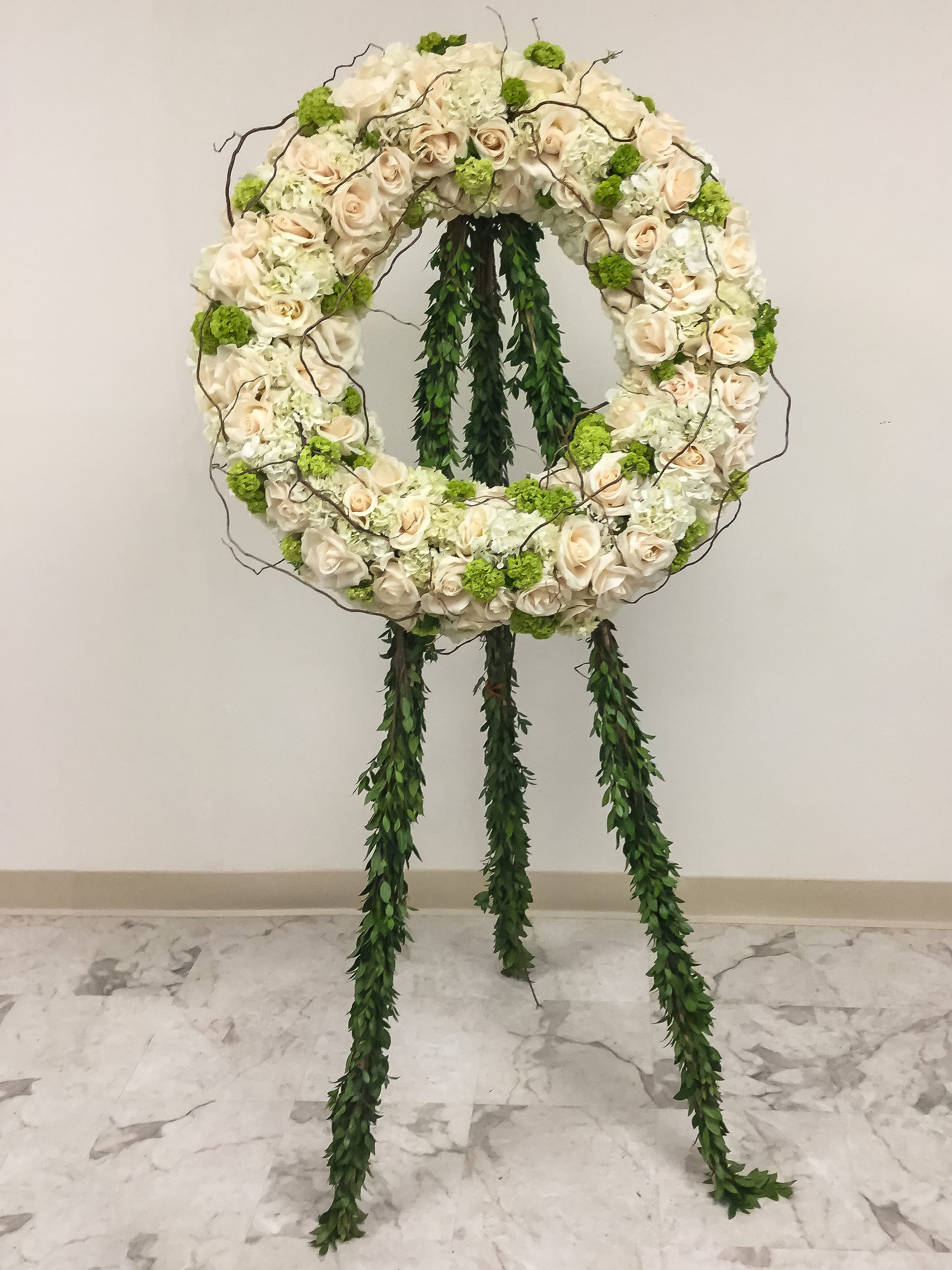 Circular floral wreath on a stand with cream roses and green accents