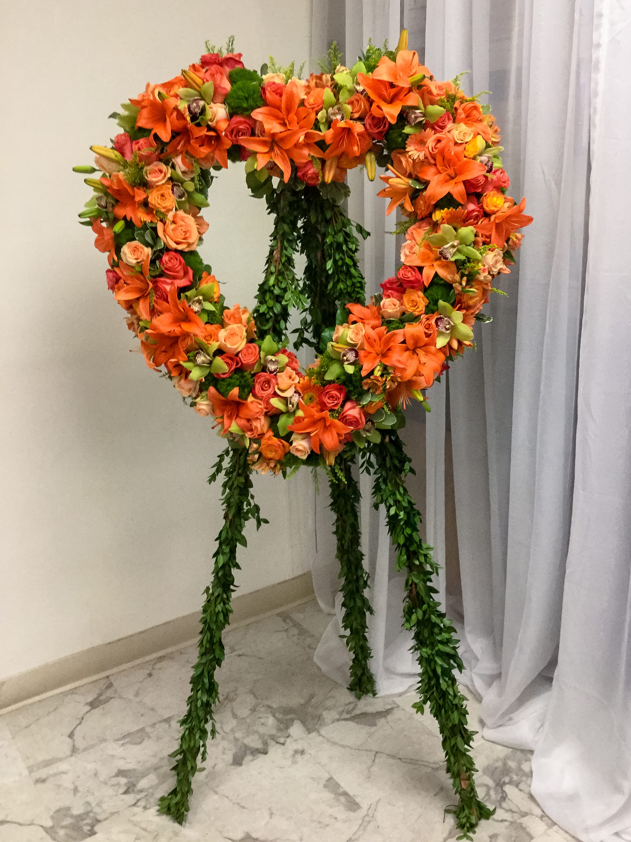 Heart-shaped floral wreath on a stand with orange and pink blooms