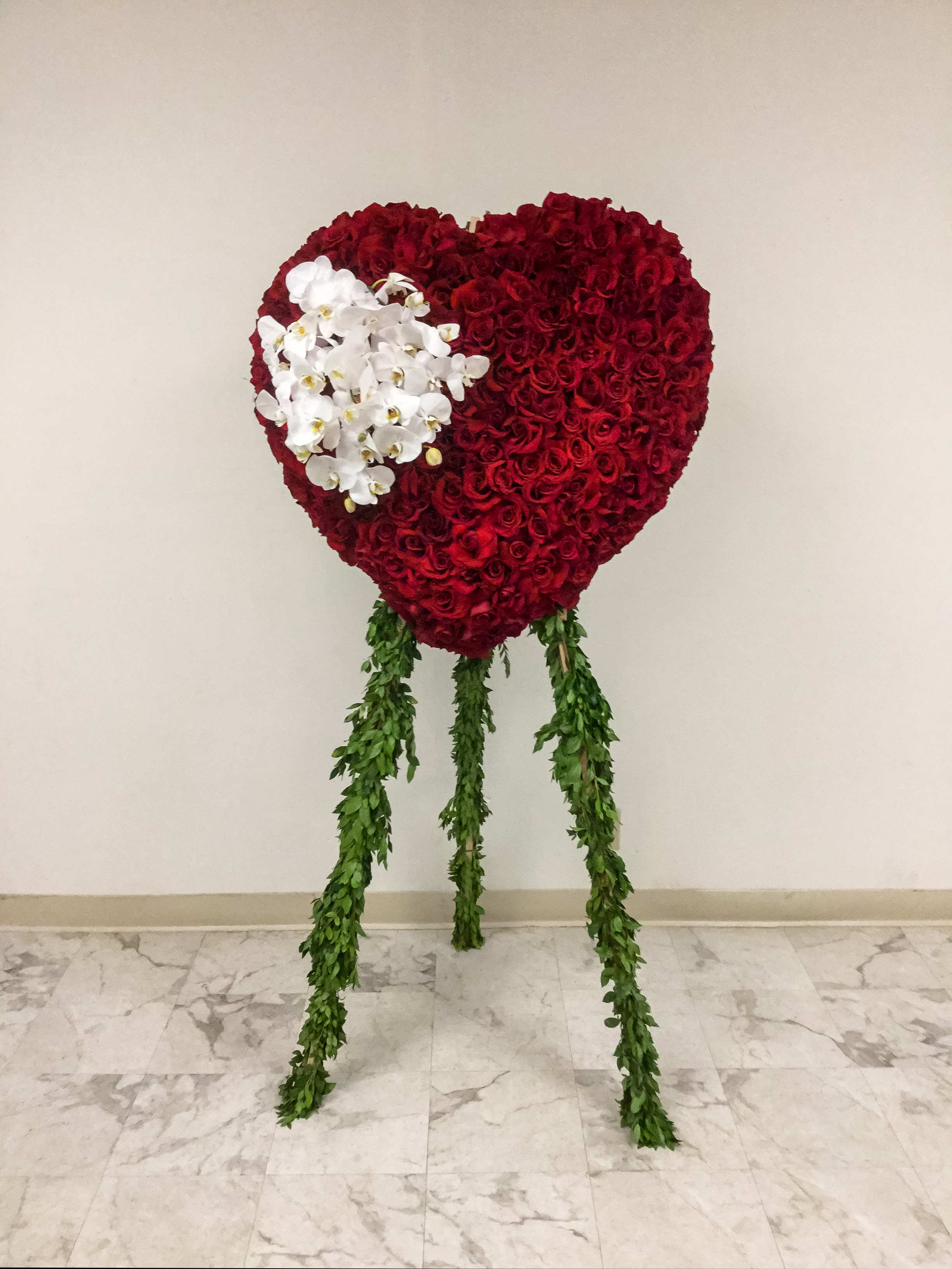 Heart-shaped red rose arrangement with white orchids and hanging greenery