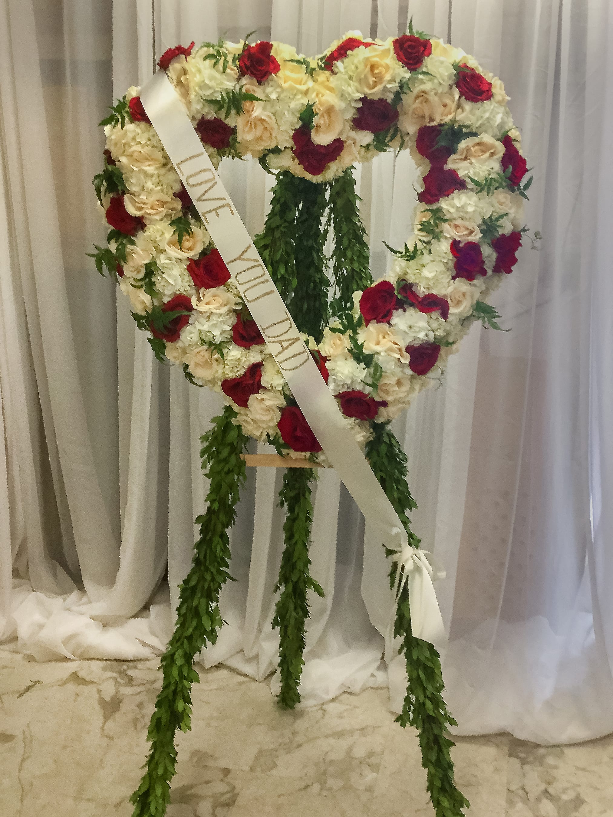 Heart-shaped rose wreath with a memorial ribbon on a stand
