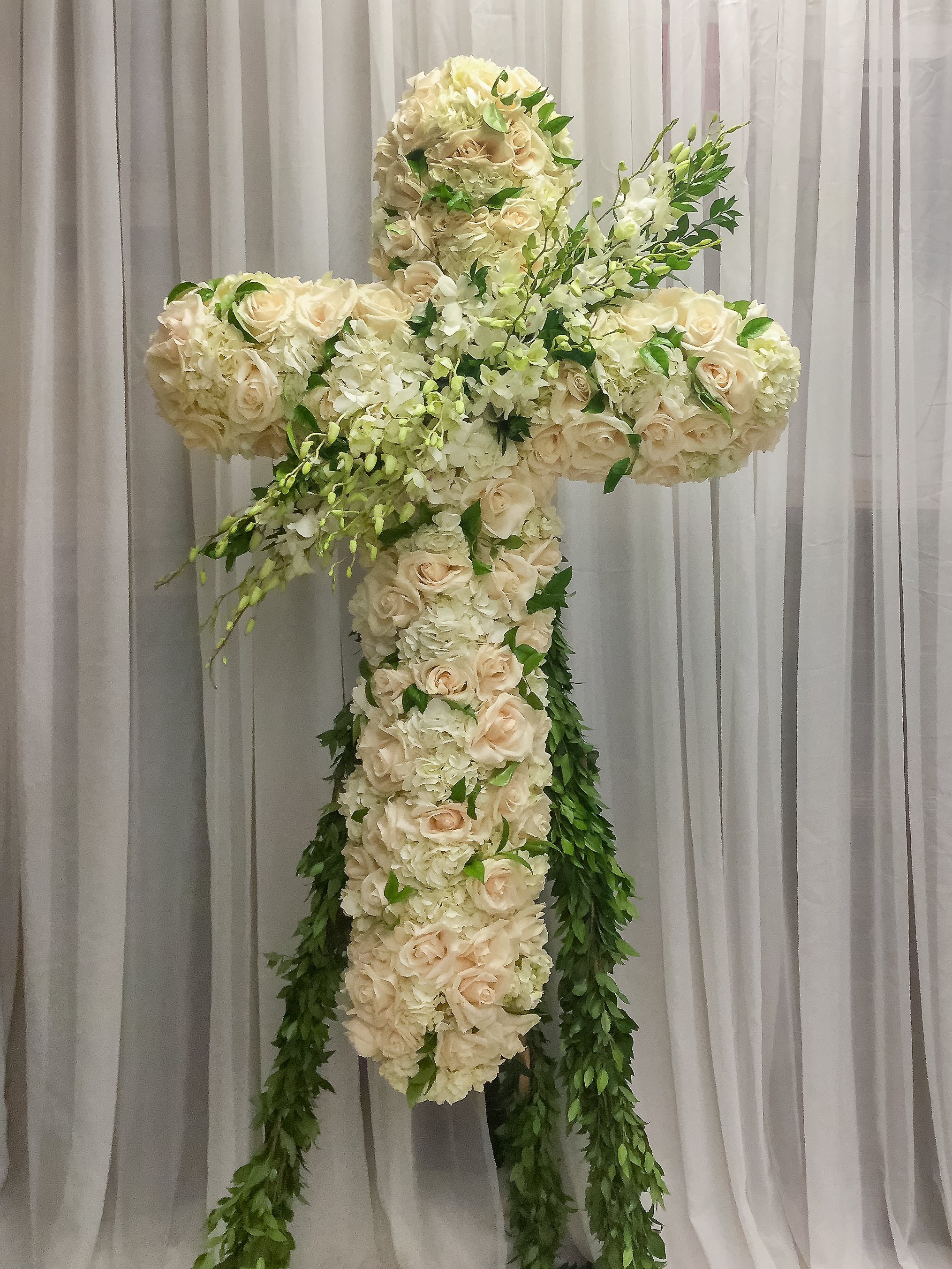 Large floral cross made of white and cream roses with trailing greenery