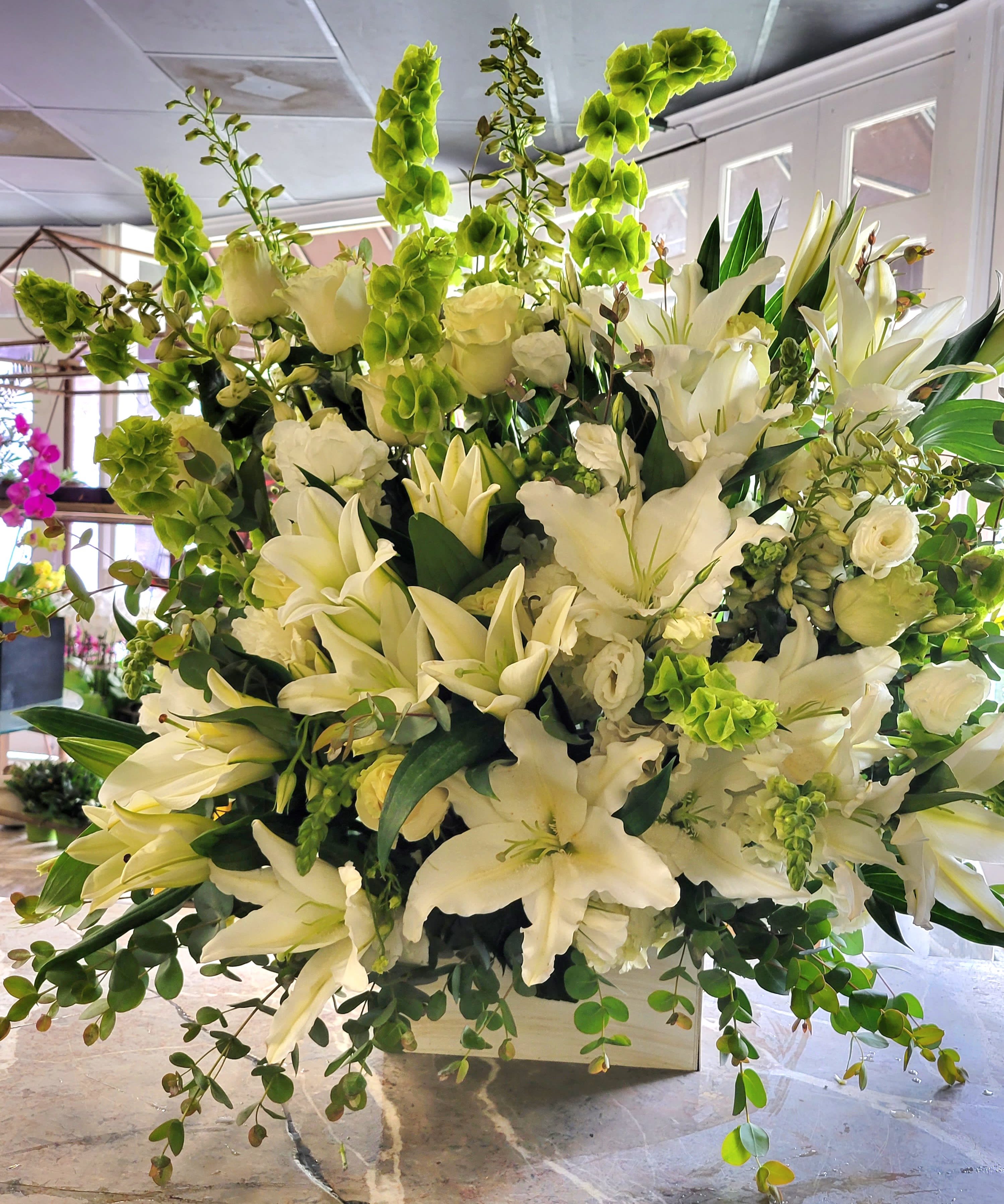 Large white floral arrangement with lilies and green accents in a white container