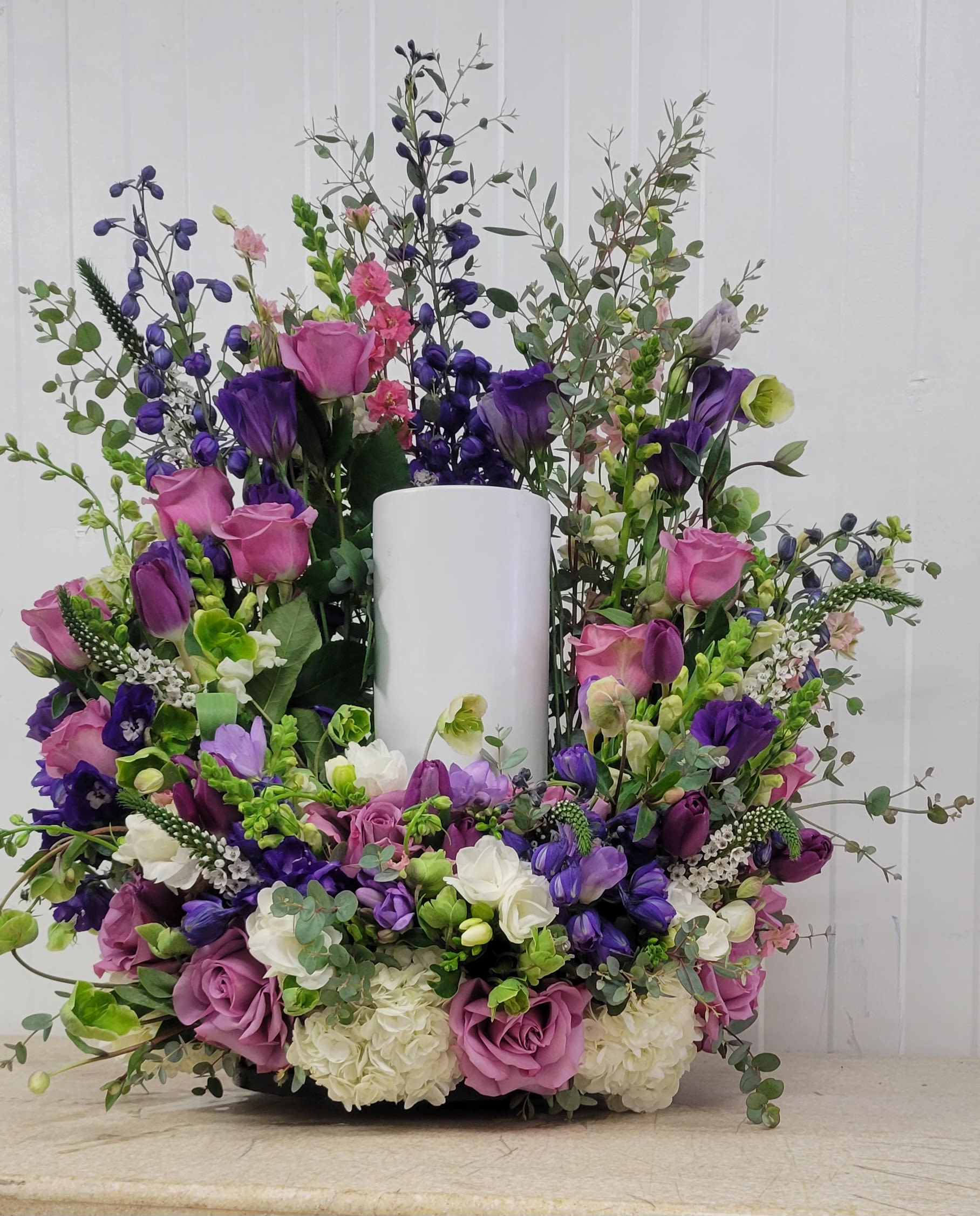 Large purple and pink floral arrangement around a white pillar candle