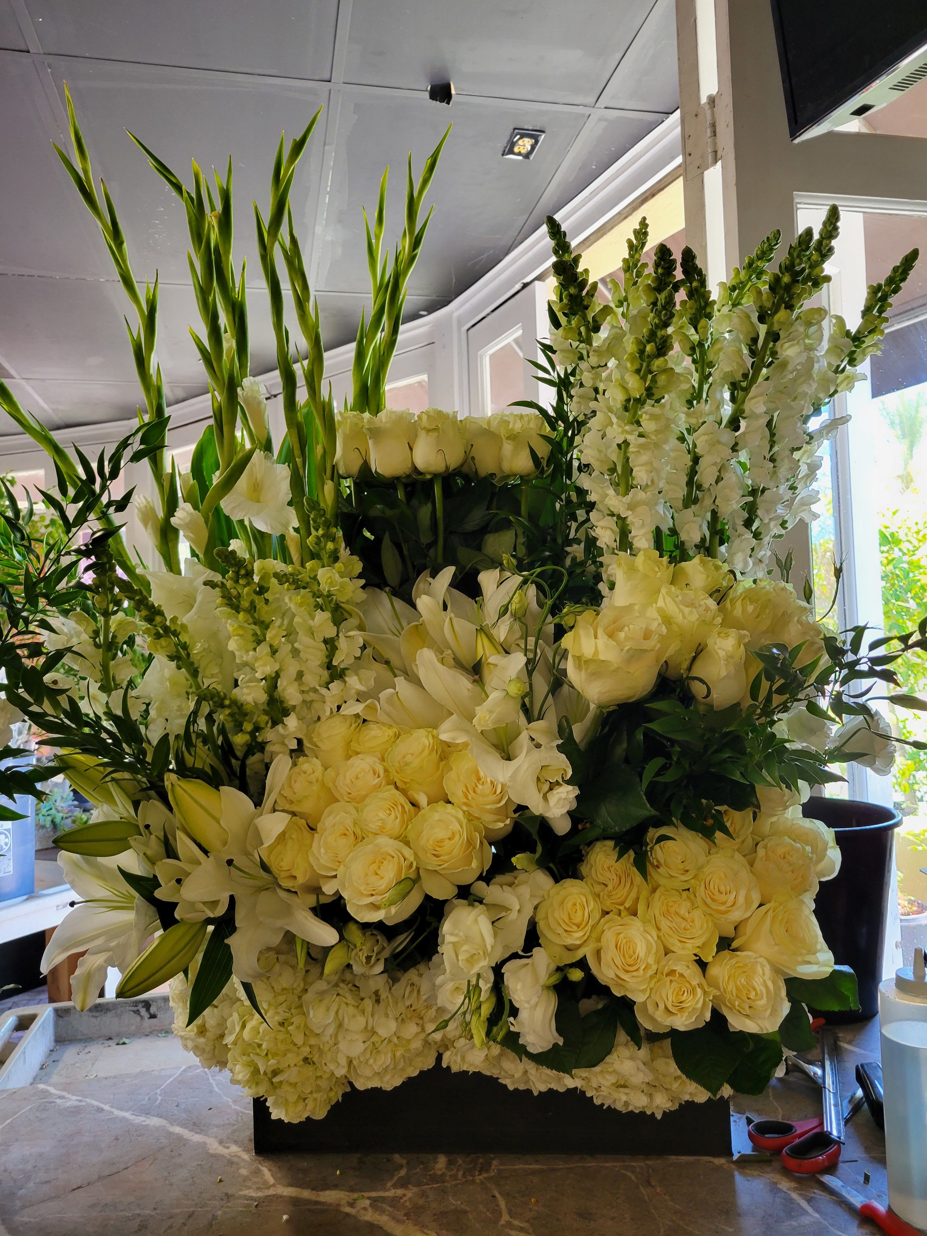 Large white floral arrangement with roses, lilies, and tall snapdragons
