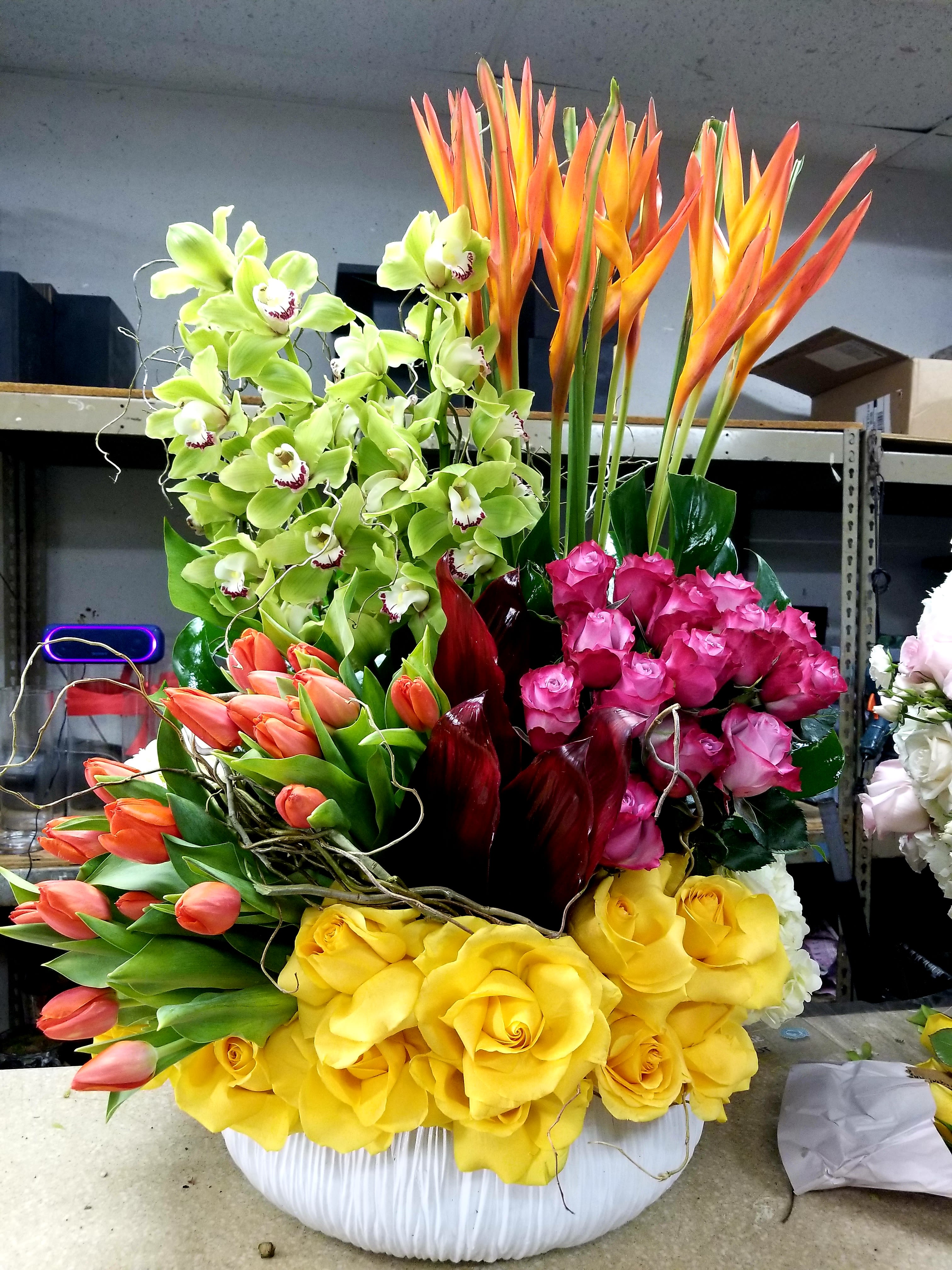 Large mixed floral arrangement with orchids, tulips, roses, and bird of paradise in a white vase