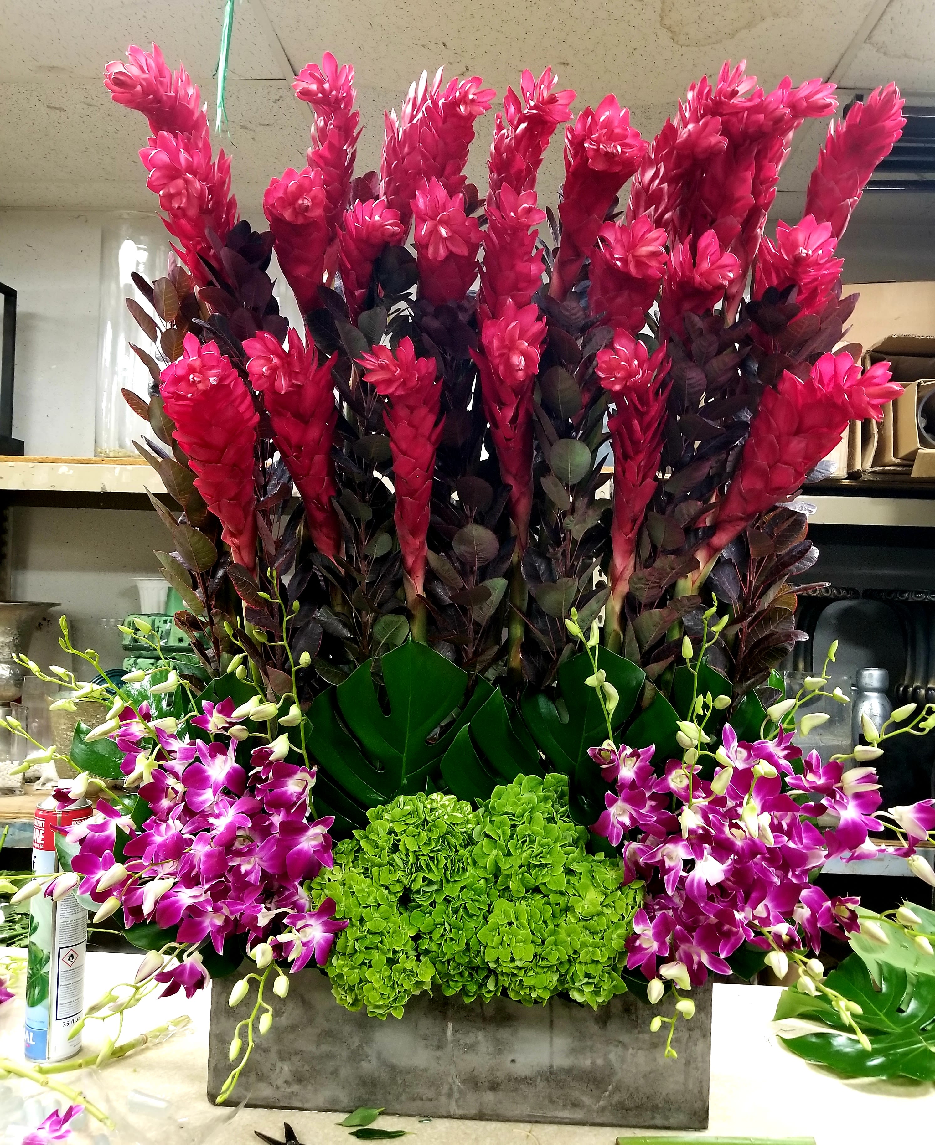 Tall floral arrangement with bright pink blooms, purple orchids, and green hydrangeas in a rectangular container