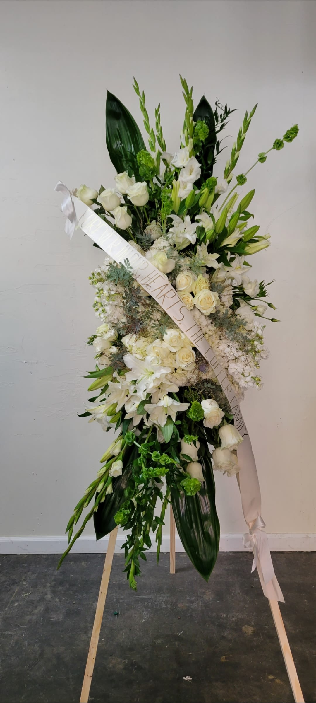 Tall white floral standing spray on an easel with a ribbon sash