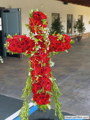 Large cross-shaped arrangement of red roses with trailing greenery