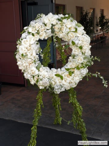 Large white floral wreath on an easel with trailing greenery