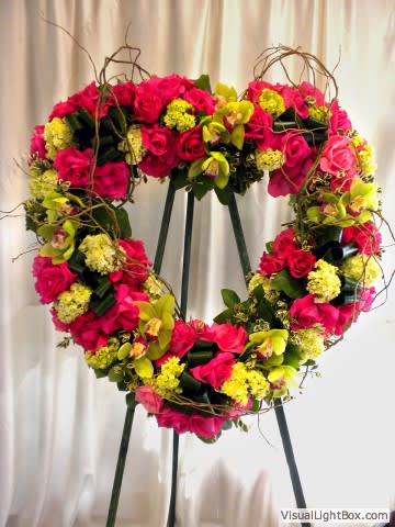 Heart-shaped floral wreath of pink roses and yellow blooms on an easel