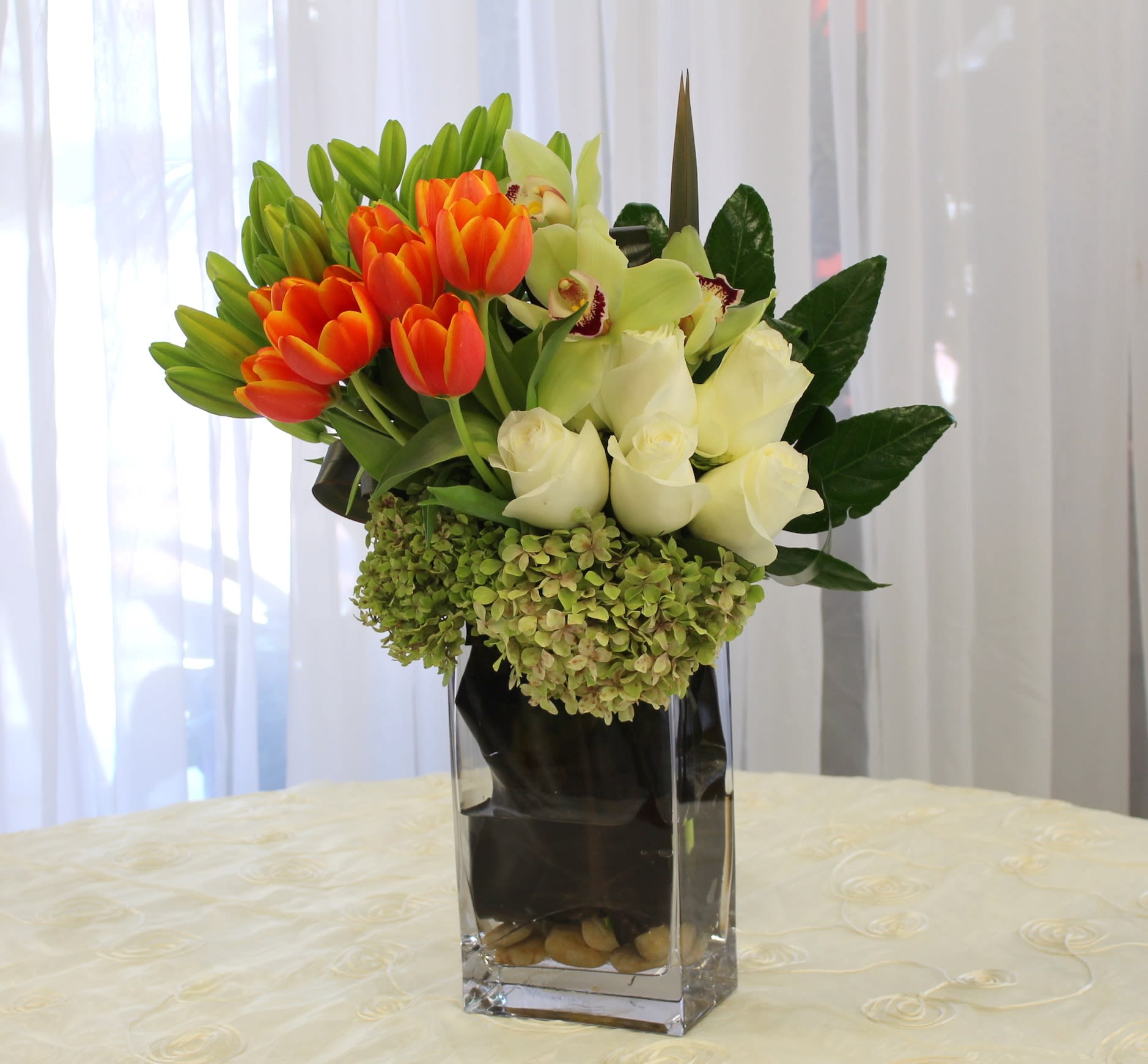 Orange tulips and white roses in a tall glass vase