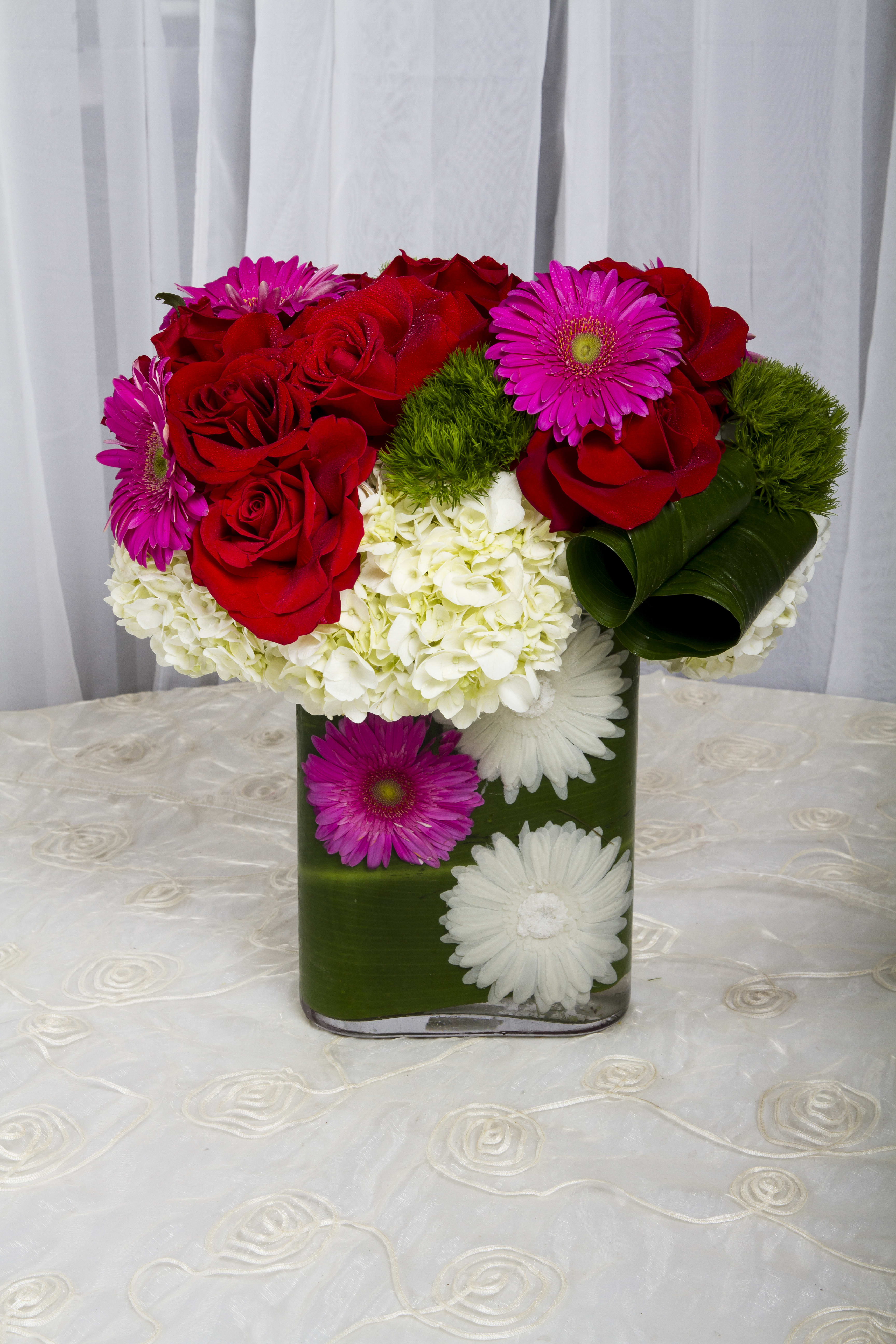 Red roses and pink daisies in a green vase with white hydrangeas