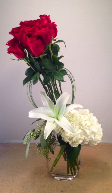 Red roses with a white lily and white hydrangea in a glass vase